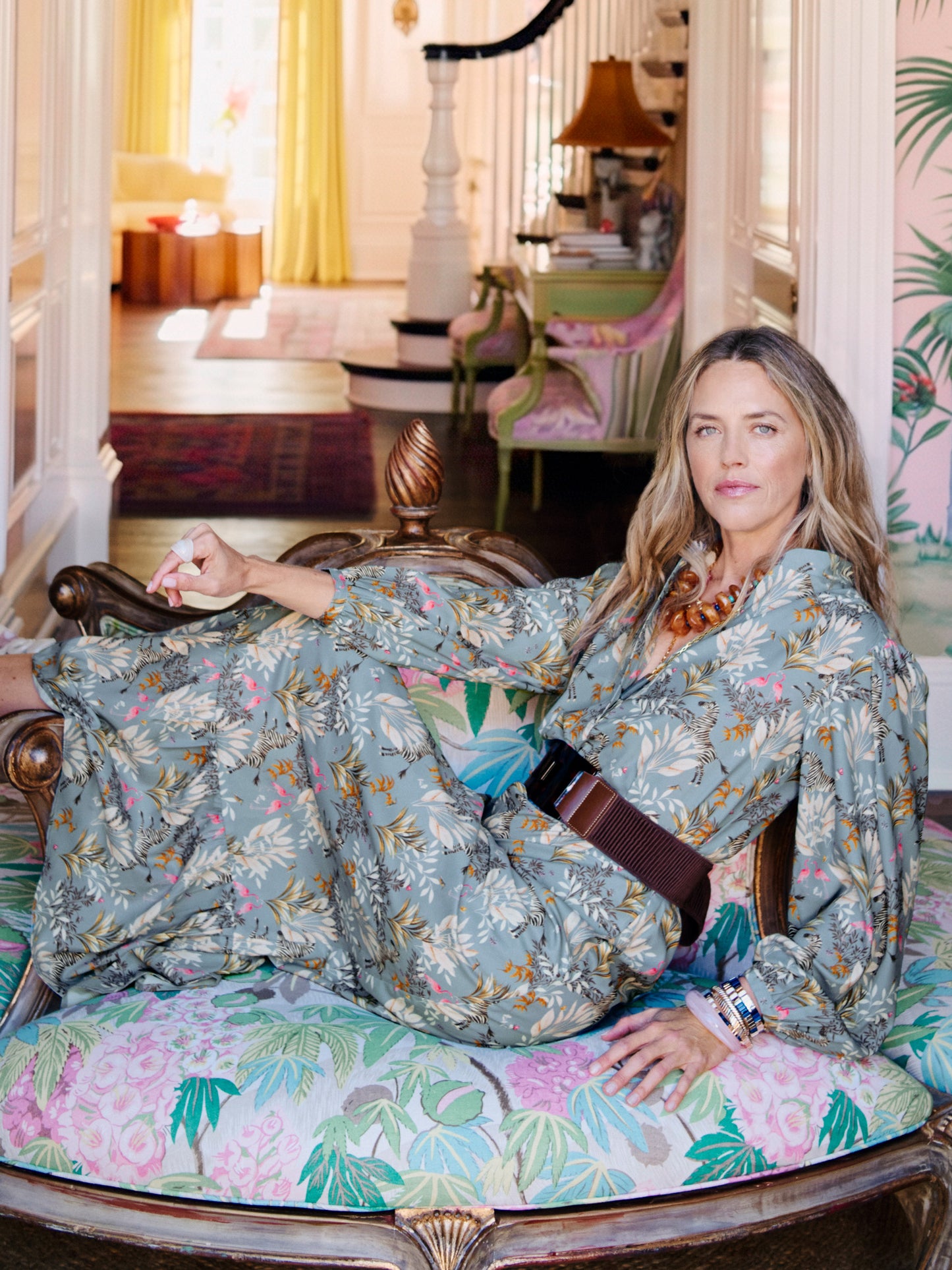 Woman lounging on a floral upholstered chair wearing the Amrita Dress in Zebra Story by J.McLaughlin, showcasing effortlessly stylish, enduring designs and innovative fabrics in a bright, elegant interior setting, embodying a legacy of timeless fashion. A destination for defining style. Life, Well-Lived.