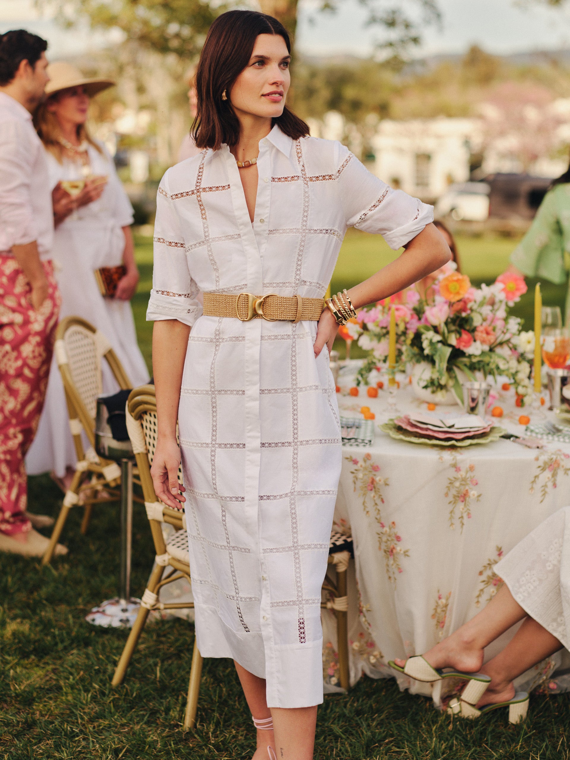 Woman wearing a Rachel Embroidered Dress by J.McLaughlin, styled with a woven belt at a garden party, showcasing effortlessly stylish, enduring designs with a legacy of timeless fashion.