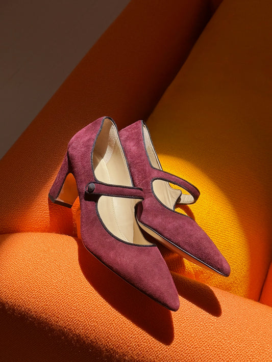 Katie Suede Pumps by J.McLaughlin in burgundy suede with pointed toes Mary Jane straps and slim heels styled on a warm orange surface