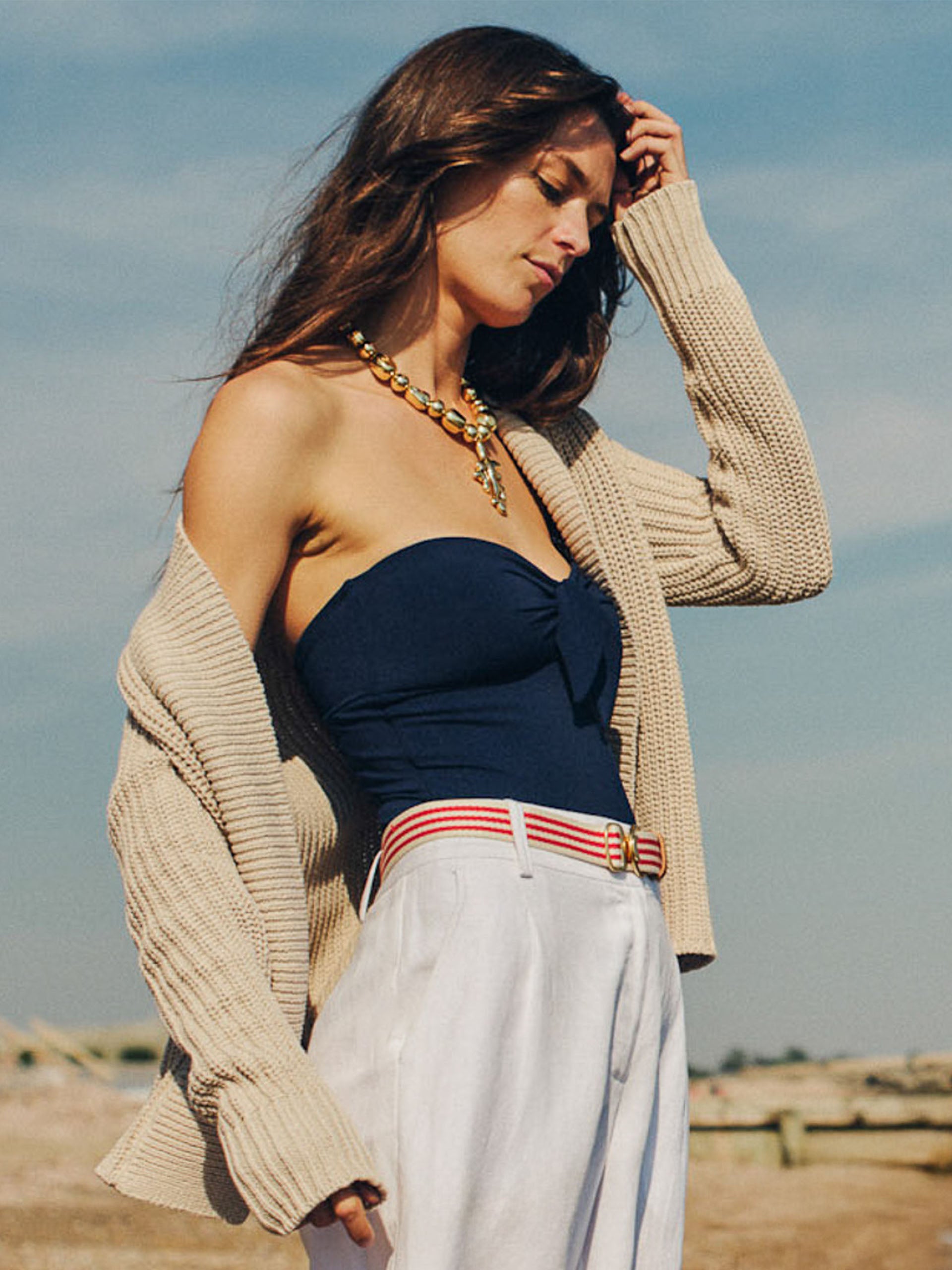 Woman wearing a beige cardigan over a navy top paired with white pants and a Mini Isobel Canvas Belt in Stripe by J.McLaughlin, showcasing effortlessly stylish, enduring designs and innovative fabrics. A destination for defining style. Life, Well-Lived.