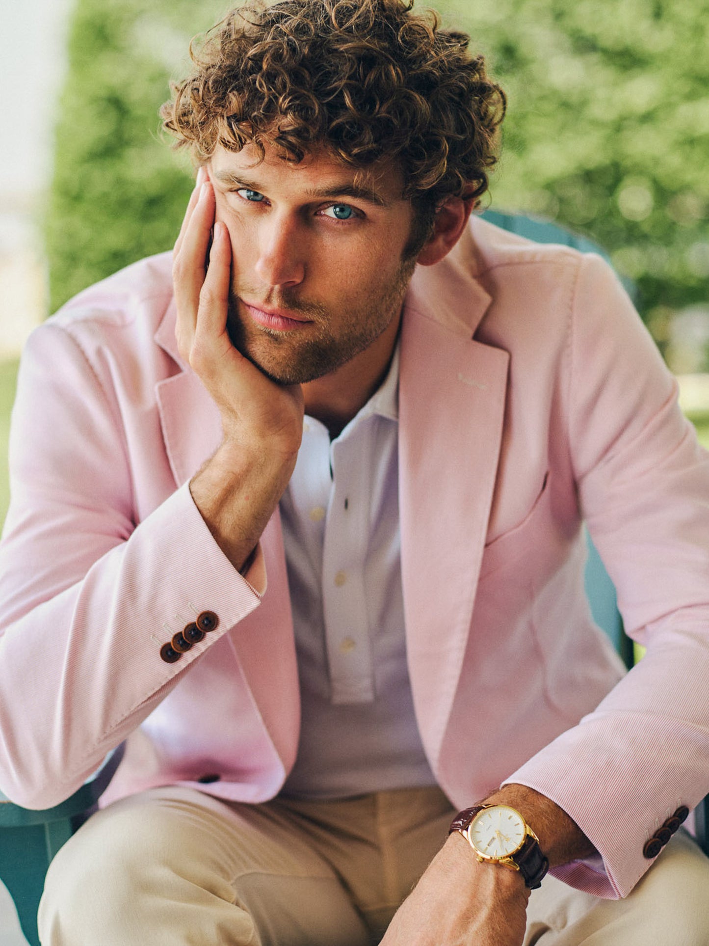 A man wearing a pale pink Suffolk Sport Coat in Fineline by J.McLaughlin with a white shirt and beige pants, showcasing effortlessly stylish and enduring designs in a timeless outdoor setting.