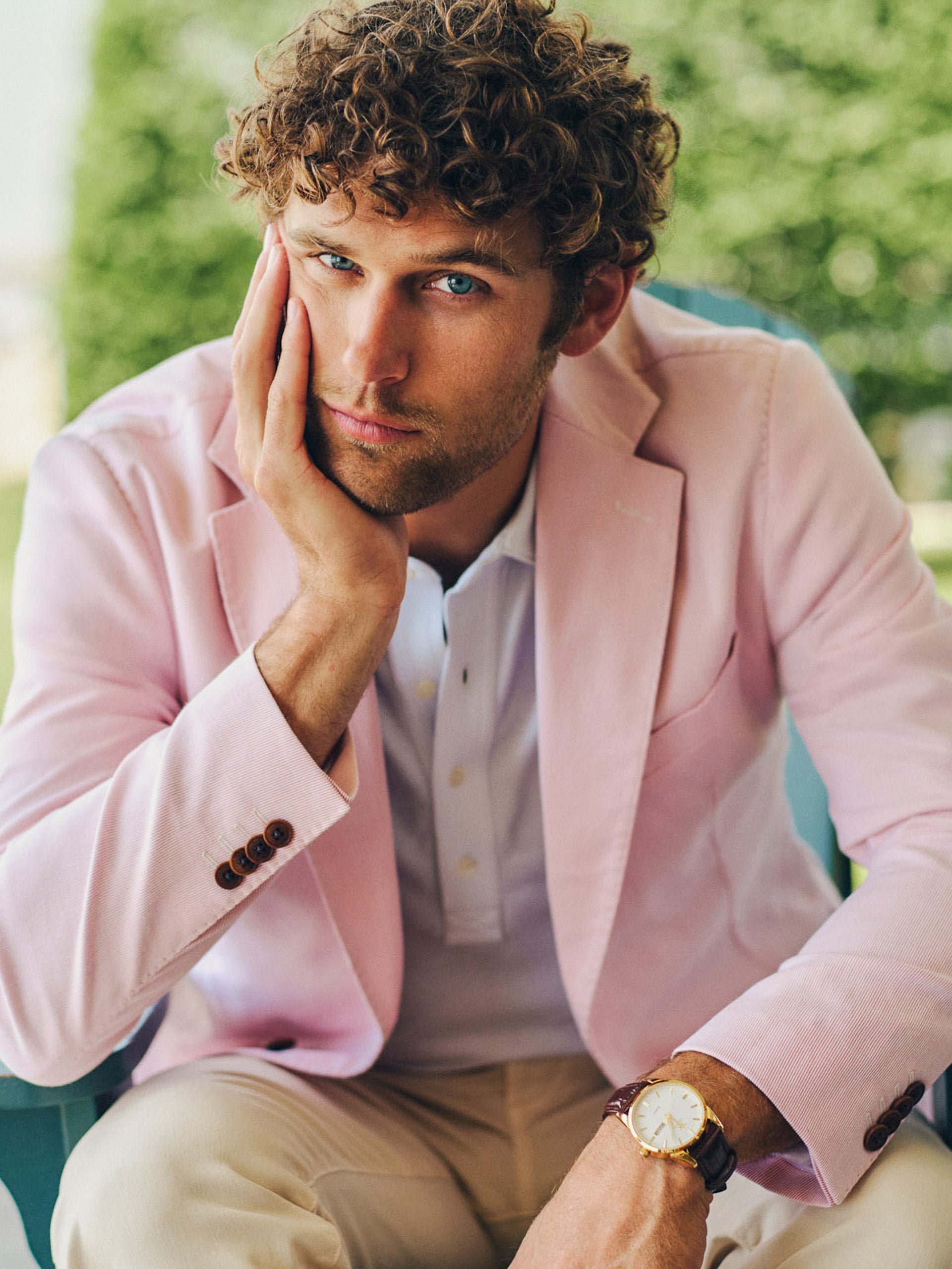 A man wearing a pale pink Suffolk Sport Coat in Fineline by J.McLaughlin with a white shirt and beige pants, showcasing effortlessly stylish and enduring designs in a timeless outdoor setting.