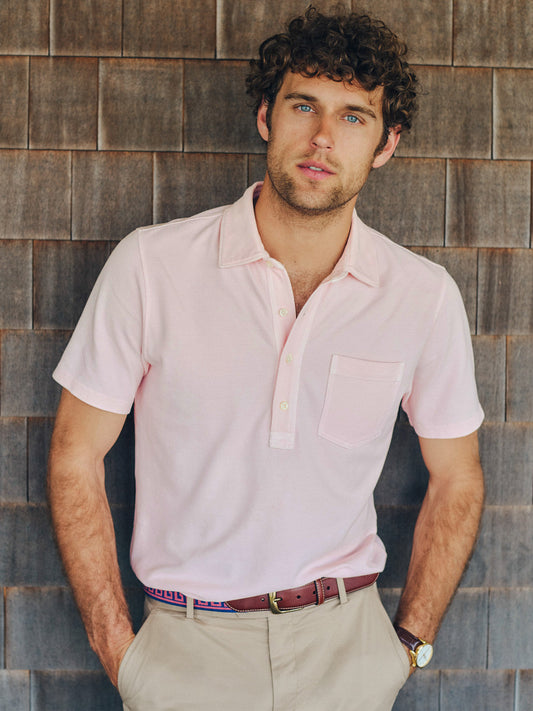Man wearing a light pink Mantle Pique Polo by J.McLaughlin paired with beige pants and a brown belt, showcasing effortlessly stylish and enduring designs in innovative fabrics.