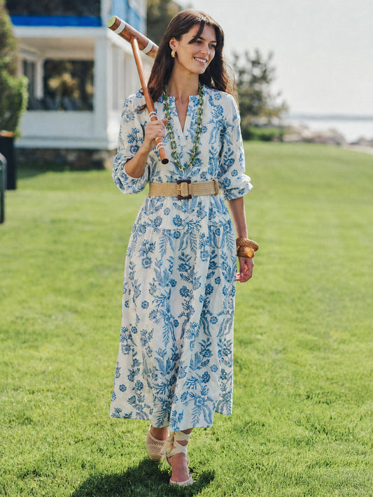 Woman wearing a Nancy Linen Blend Embroidered Dress in white with blue floral patterns, accessorized with a belt and jewelry, smiling outdoors with a croquet mallet, showcasing J.McLaughlin’s effortlessly stylish, enduring designs and innovative fabrics, embodying a legacy of timeless fashion. A destination for defining style. Life, Well-Lived.