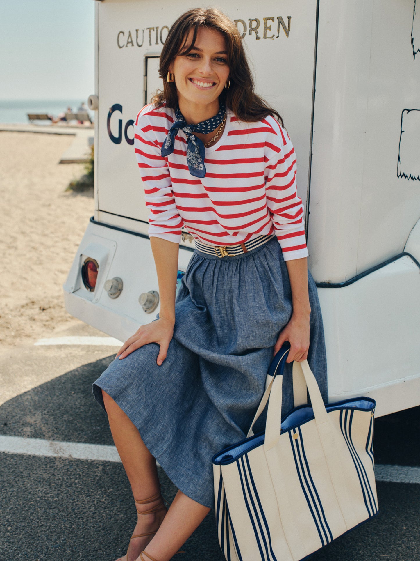Woman wearing a Nico Tee in Stripe by J.McLaughlin with red and white stripes, paired with a blue skirt and striped tote bag, embodying effortlessly stylish, enduring designs.