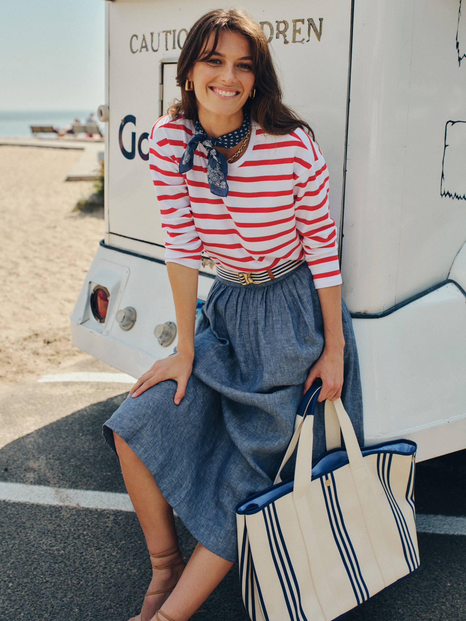 Woman wearing a red and white striped top with a blue skirt and neck scarf, carrying the Alma Canvas Tote in Stripe by J.McLaughlin, showcasing effortlessly stylish, enduring designs.