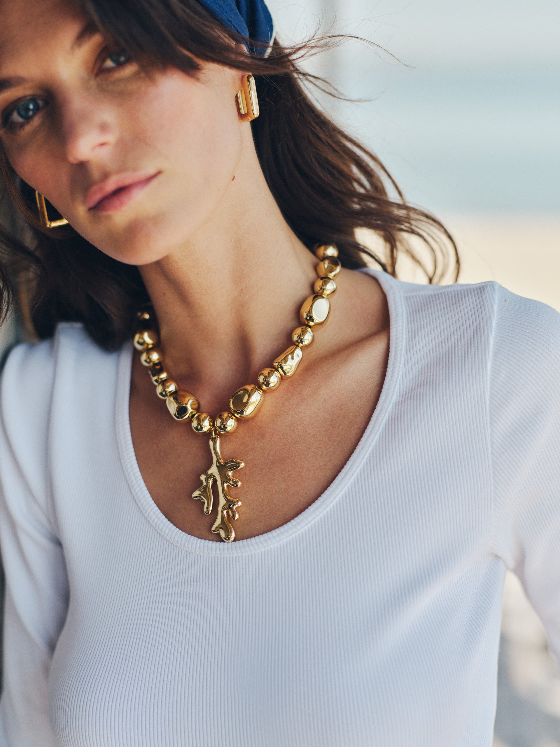 Close-up of a woman wearing a gold statement Coral Necklace by J.McLaughlin paired with gold earrings and a white top, showcasing effortlessly stylish, enduring designs and innovative craftsmanship.