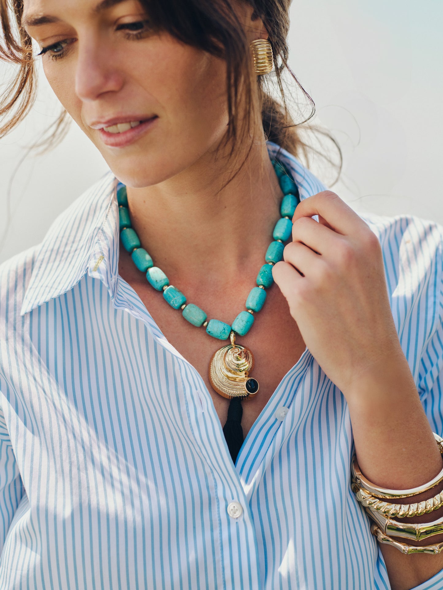 Woman wearing a blue and white striped blouse accessorized with a Shell & Tassel Necklace by J.McLaughlin, featuring turquoise beads and gold accents, embodying effortlessly stylish, enduring designs and a legacy of timeless fashion. A destination for defining style. Life, Well-Lived.