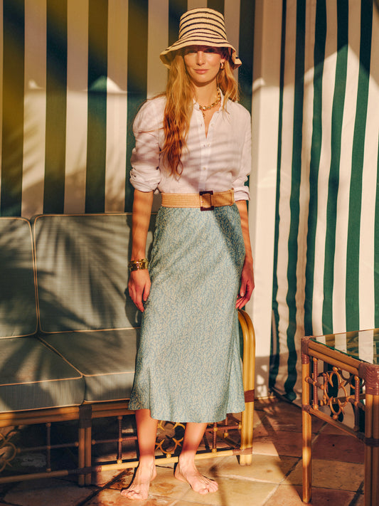 Woman wearing a white blouse and Adelyn Silk Blend Skirt in Mini Sea Vine Bias by J.McLaughlin, paired with a striped hat and belt, showcasing effortlessly stylish, enduring designs.