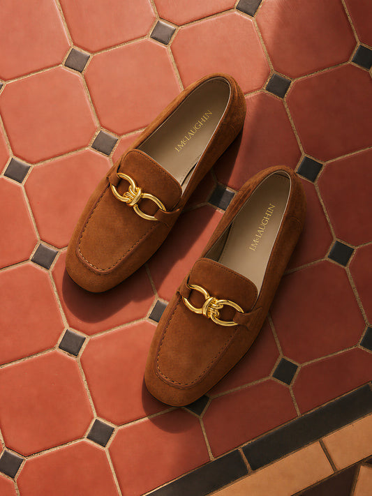 Pair of brown Mila Suede Loafers by J.McLaughlin with gold-tone hardware, displayed on a patterned terracotta tile floor, embodying effortless style.