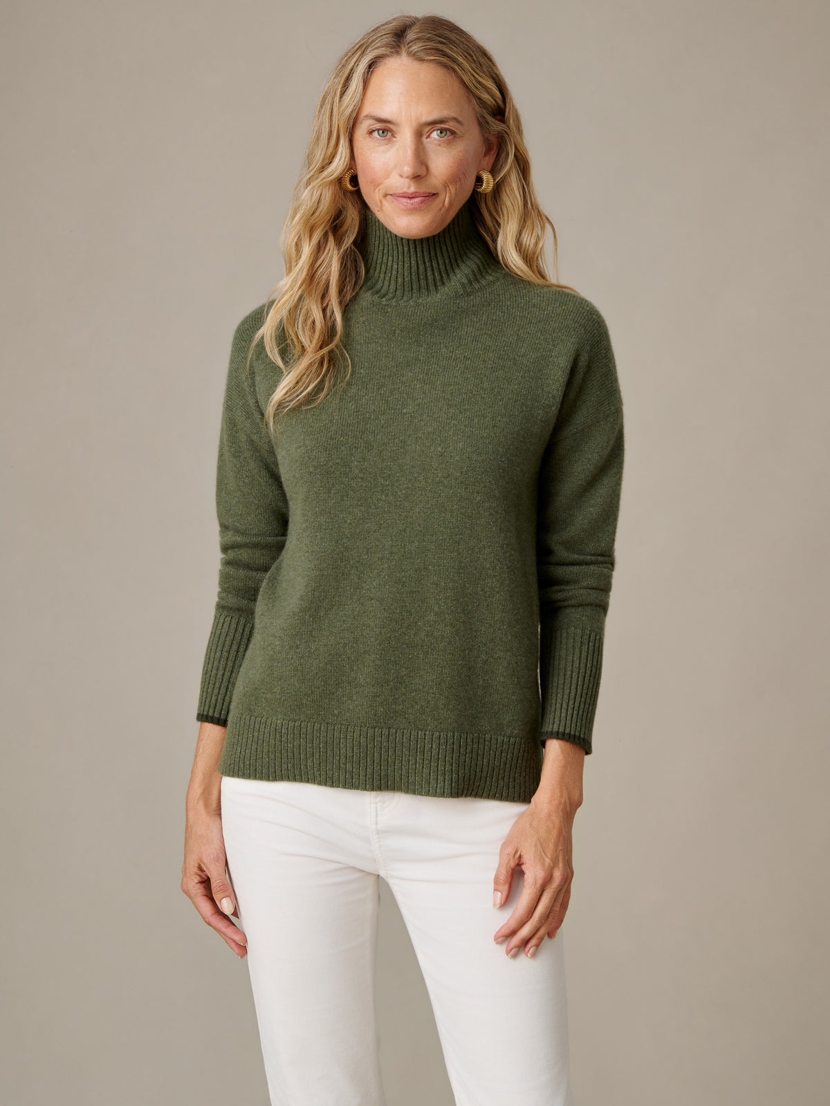 Woman wearing the Dina Cashmere Turtleneck in olive green with white pants showcasing its soft cashmere knit and timeless turtleneck design