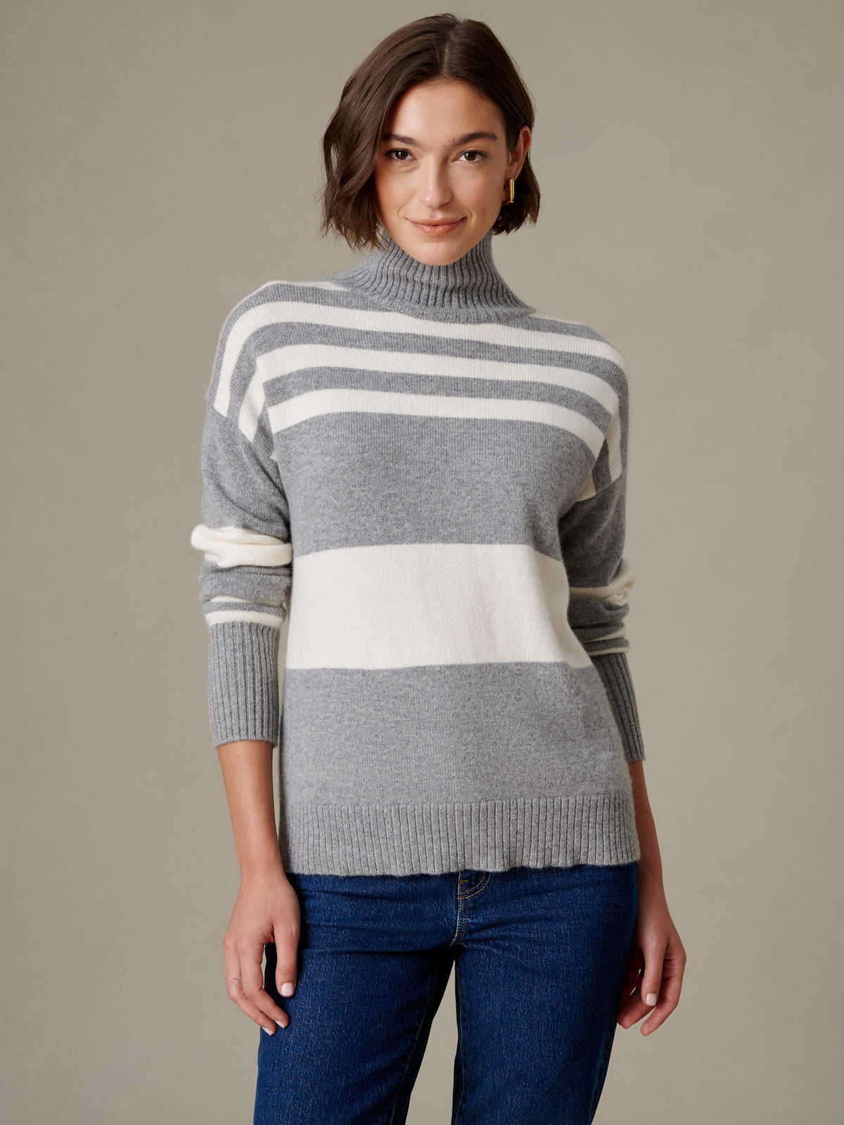 Dina Cashmere Turtleneck in Stripe by J.McLaughlin modeled by a woman in a soft gray and cream striped cashmere sweater with jeans