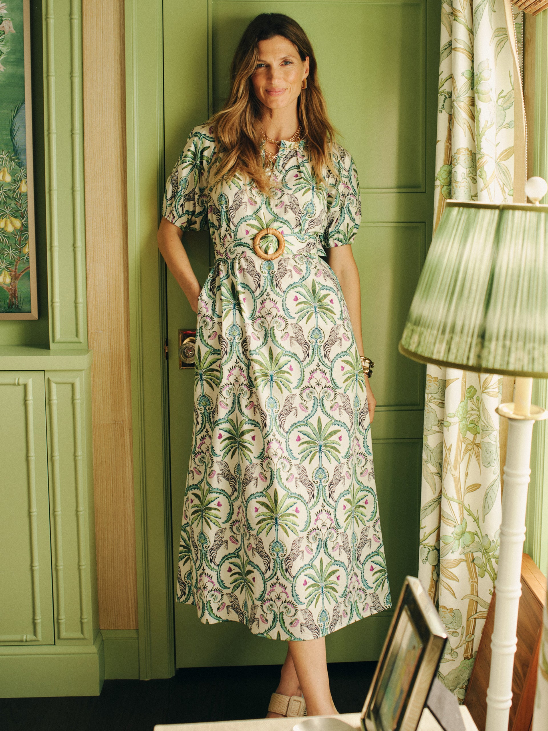 Woman wearing Marley Dress in Zebra Isle by J.McLaughlin featuring elegant green botanical print, standing in a stylish room with green walls and soft natural light, embodying effortlessly stylish, enduring designs with a legacy of timeless fashion, a destination for defining style. Life, Well-Lived.