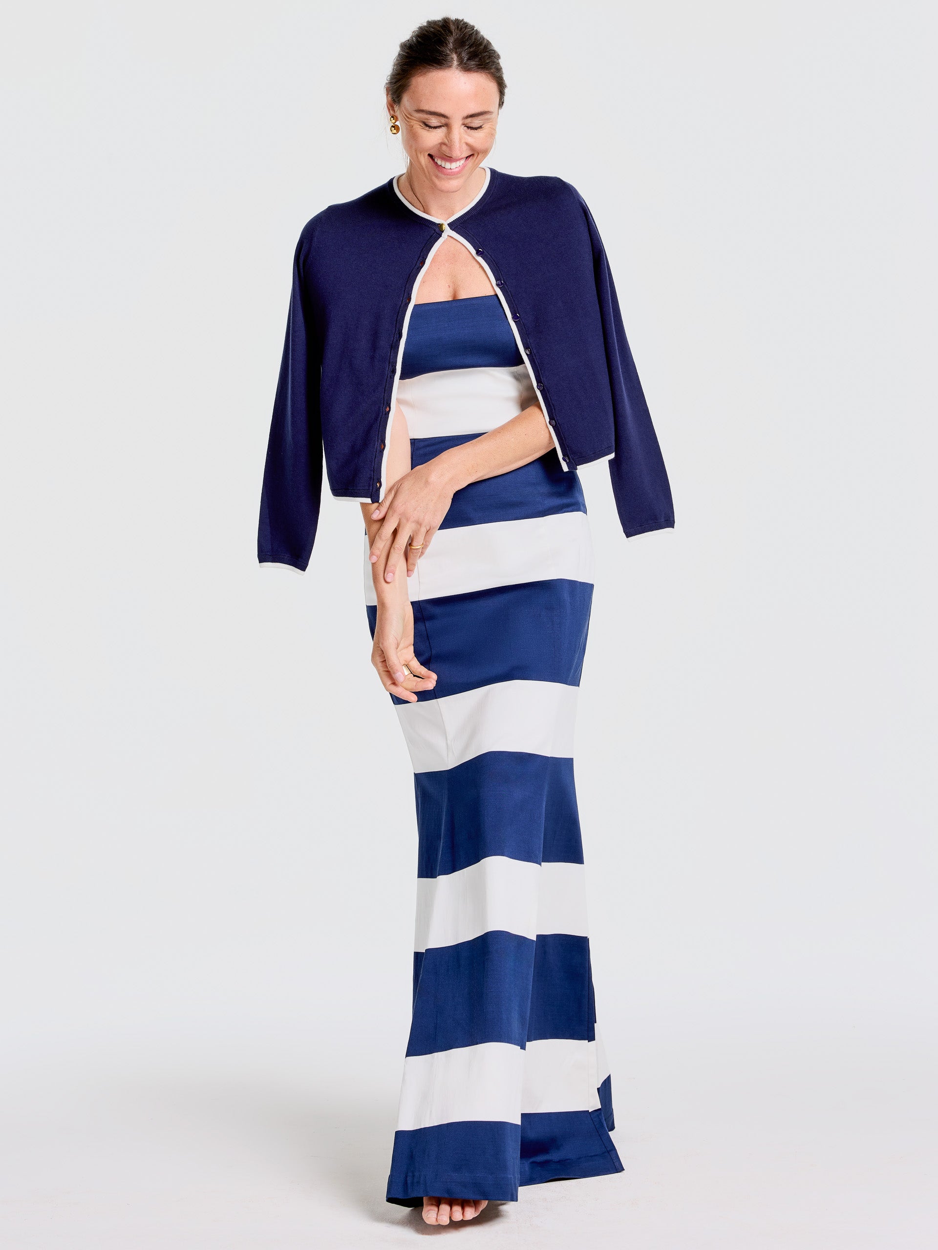 Woman wearing a navy Aileen Cardigan by J.McLaughlin over a blue and white striped dress, showcasing effortlessly stylish layering and enduring designs for a life well-lived.