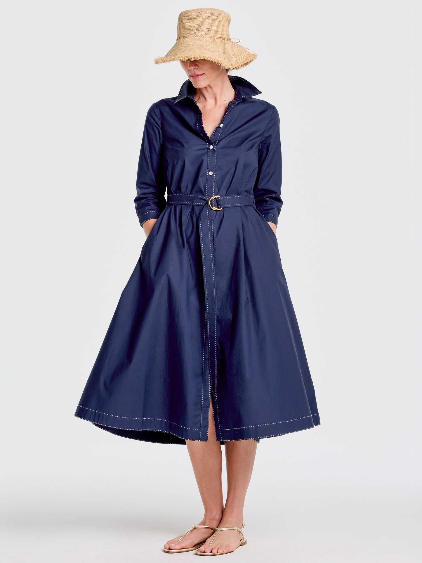 Woman wearing a navy Stephanie Dress by J.McLaughlin, styled with a wide-brimmed straw hat and sandals, showcasing effortlessly stylish, enduring designs in innovative fabrics.