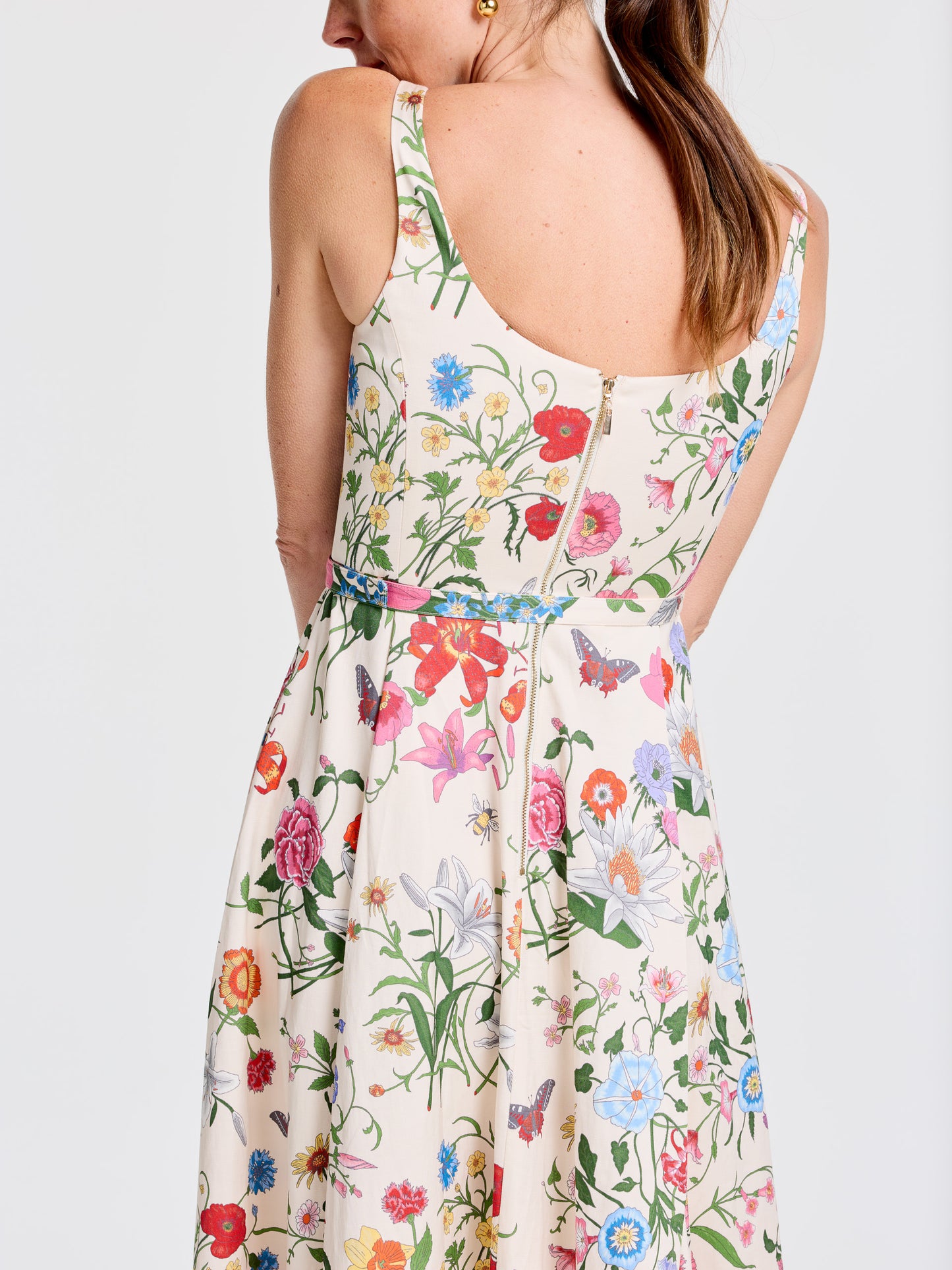 Woman wearing a sleeveless Charlotte Dress in Dragonfly Garden by J.McLaughlin, featuring a floral pattern with vibrant flowers and butterflies, showcasing effortlessly stylish, enduring designs and innovative fabrics for a legacy of timeless fashion. A destination for defining style. Life, Well-Lived.