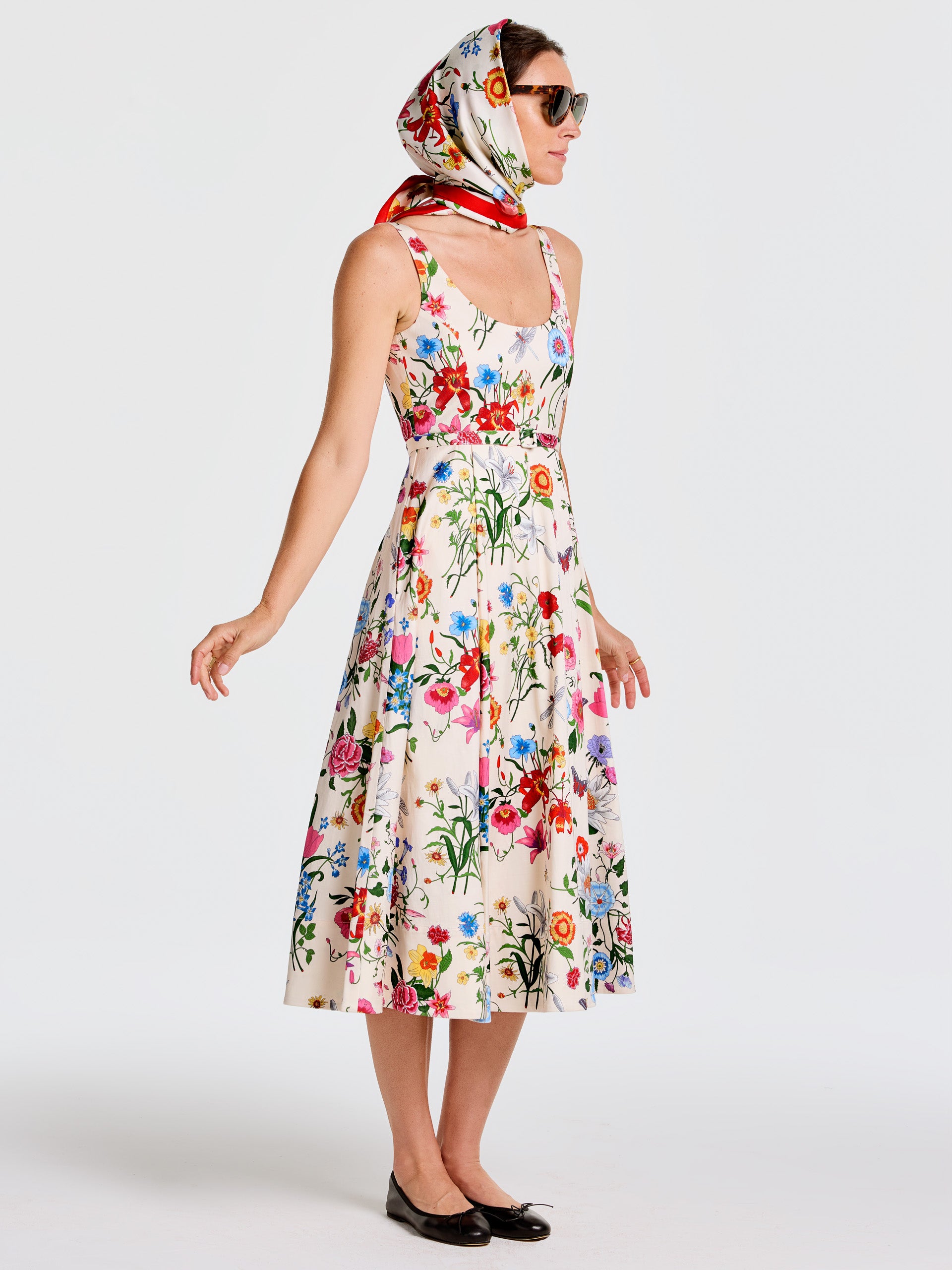 Woman wearing the Charlotte Dress in Dragonfly Garden by J.McLaughlin, featuring a vibrant floral pattern, paired with a colorful scarf and sunglasses, embodying effortlessly stylish, enduring designs.