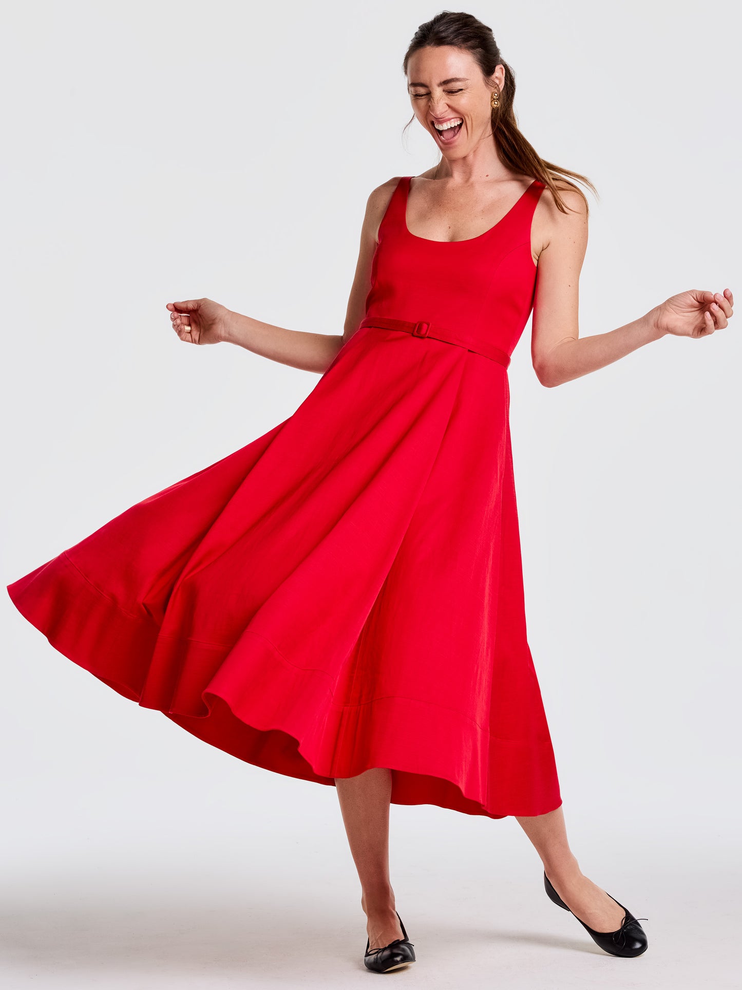 Woman joyfully twirling in a vibrant red Charlotte Dress by J.McLaughlin, showcasing effortlessly stylish, enduring designs in an innovative fabric for a legacy of timeless fashion.