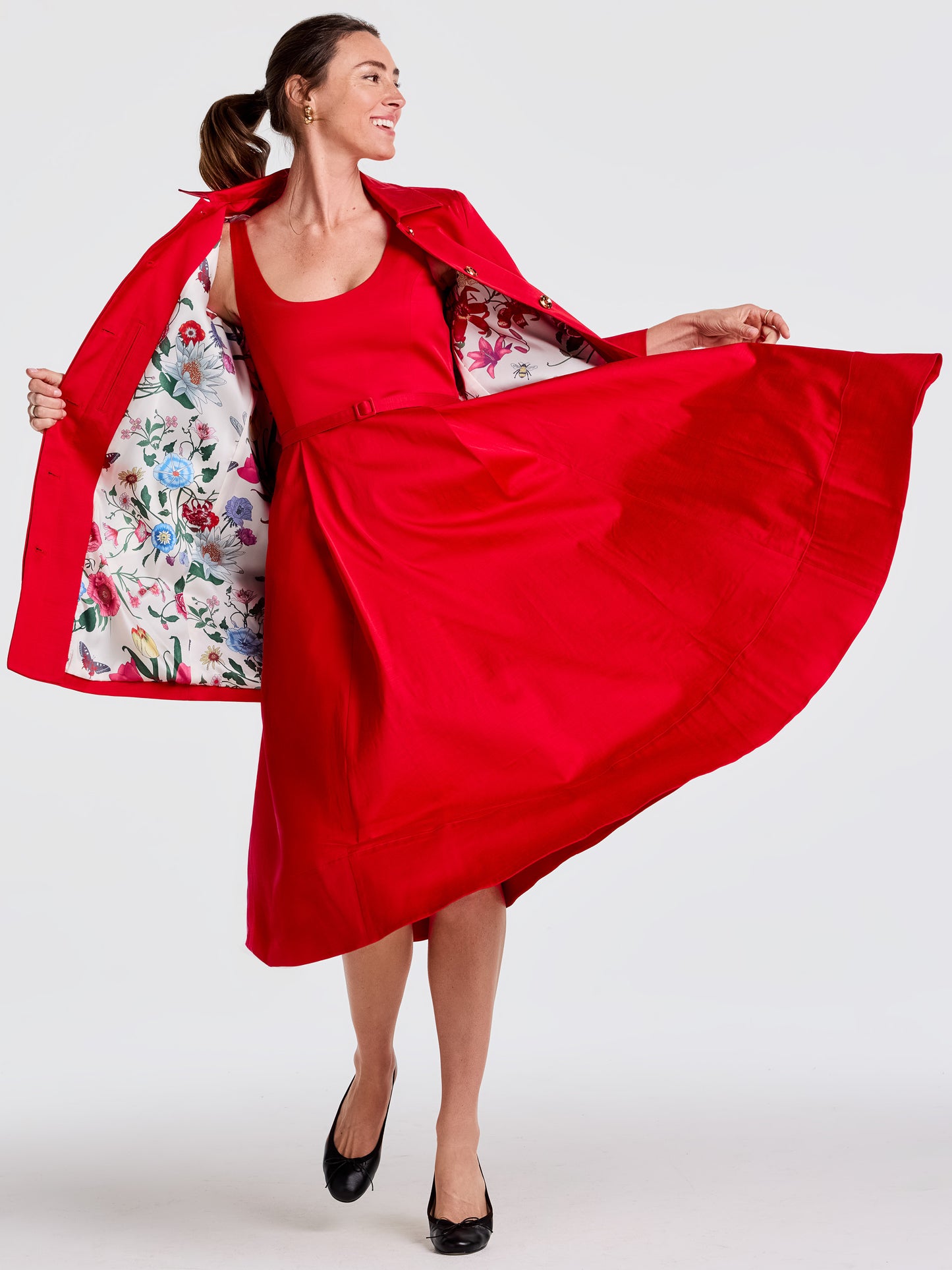 Woman wearing a vibrant red Emma Coat by J.McLaughlin with a floral lining, paired with a red dress and black shoes, showcasing effortlessly stylish, enduring designs and a legacy of timeless fashion. A destination for defining style. Life, Well-Lived.