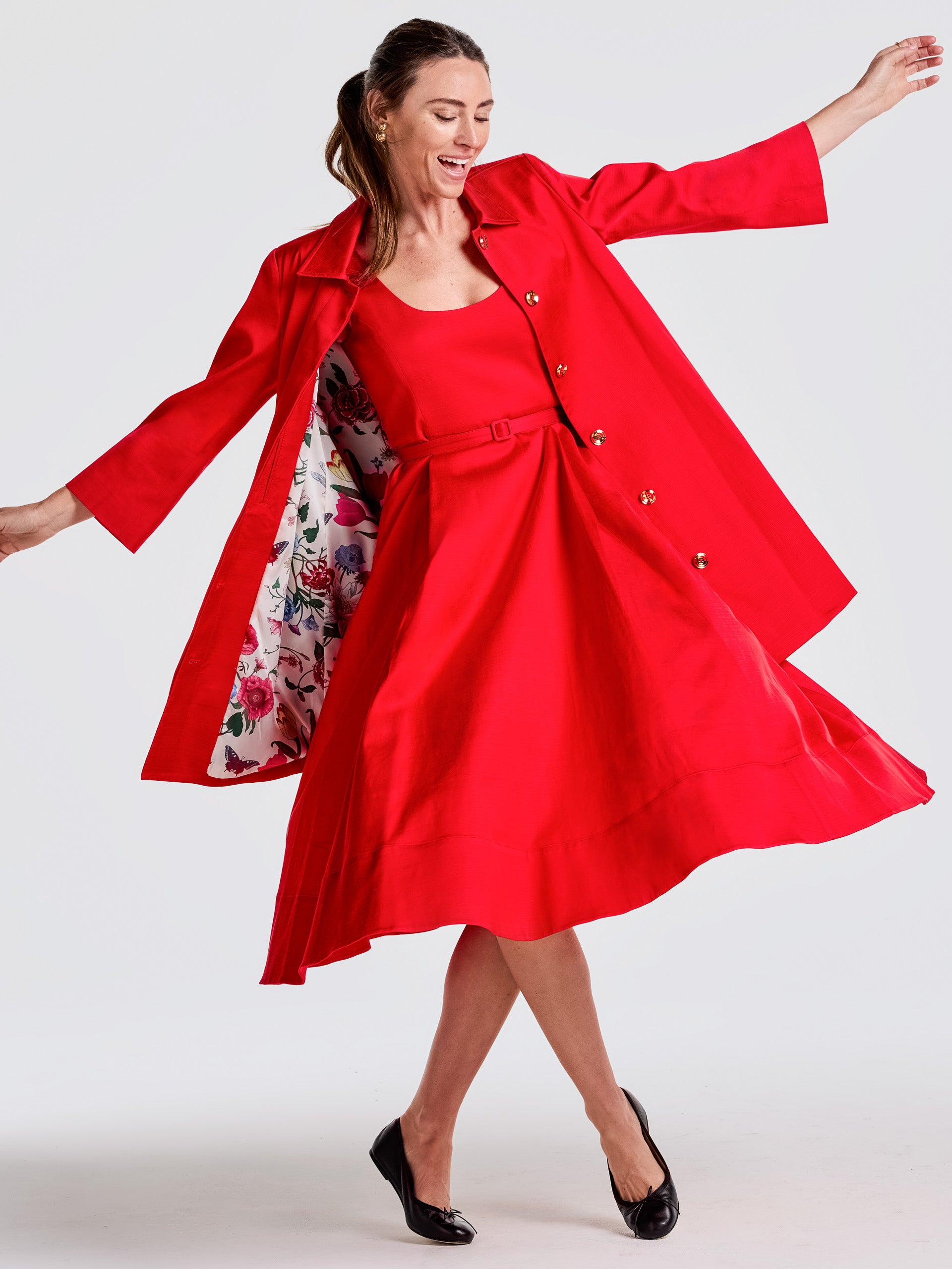 Woman twirling in a vibrant red Charlotte Dress paired with a matching coat featuring a floral lining, showcasing J.McLaughlin's effortlessly stylish and enduring designs.