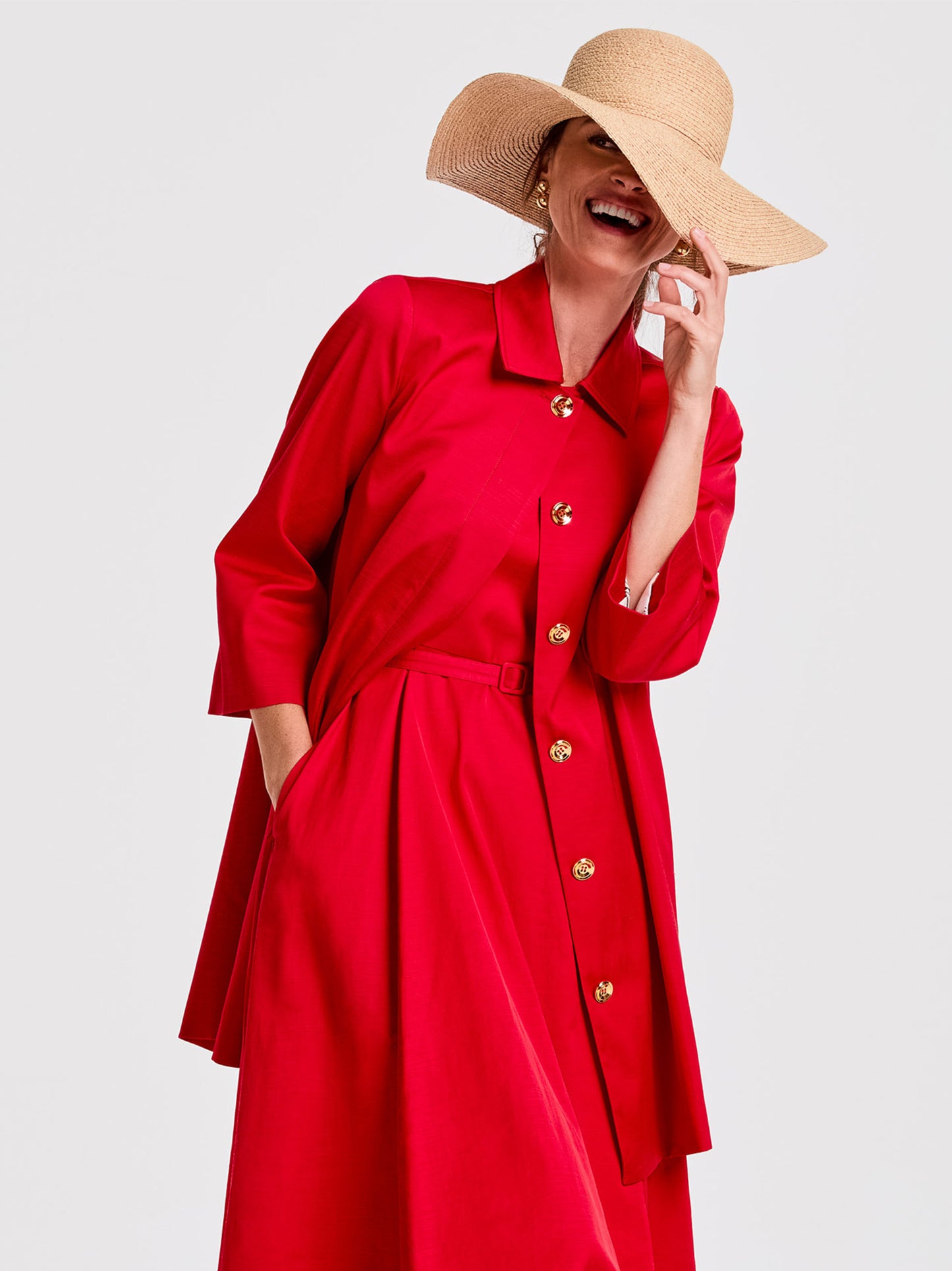 Woman wearing a vibrant red Emma Coat by J.McLaughlin styled with a wide-brimmed natural straw hat, showcasing effortlessly stylish, enduring designs and innovative fabrics.