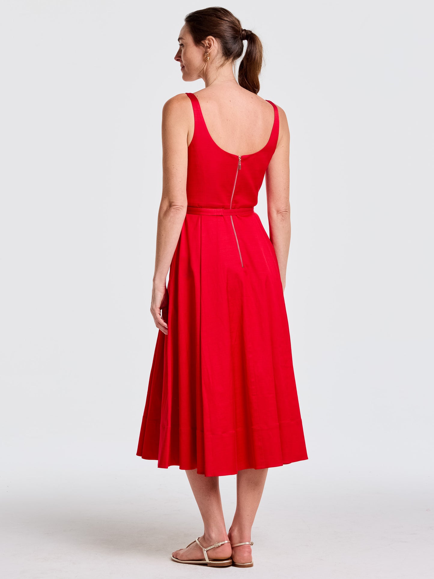 Woman wearing a sleeveless red Charlotte Dress by J.McLaughlin, showcasing an effortlessly stylish and enduring design with a fitted waist and flared skirt, embodying a legacy of timeless fashion. A destination for defining style. Life, Well-Lived.