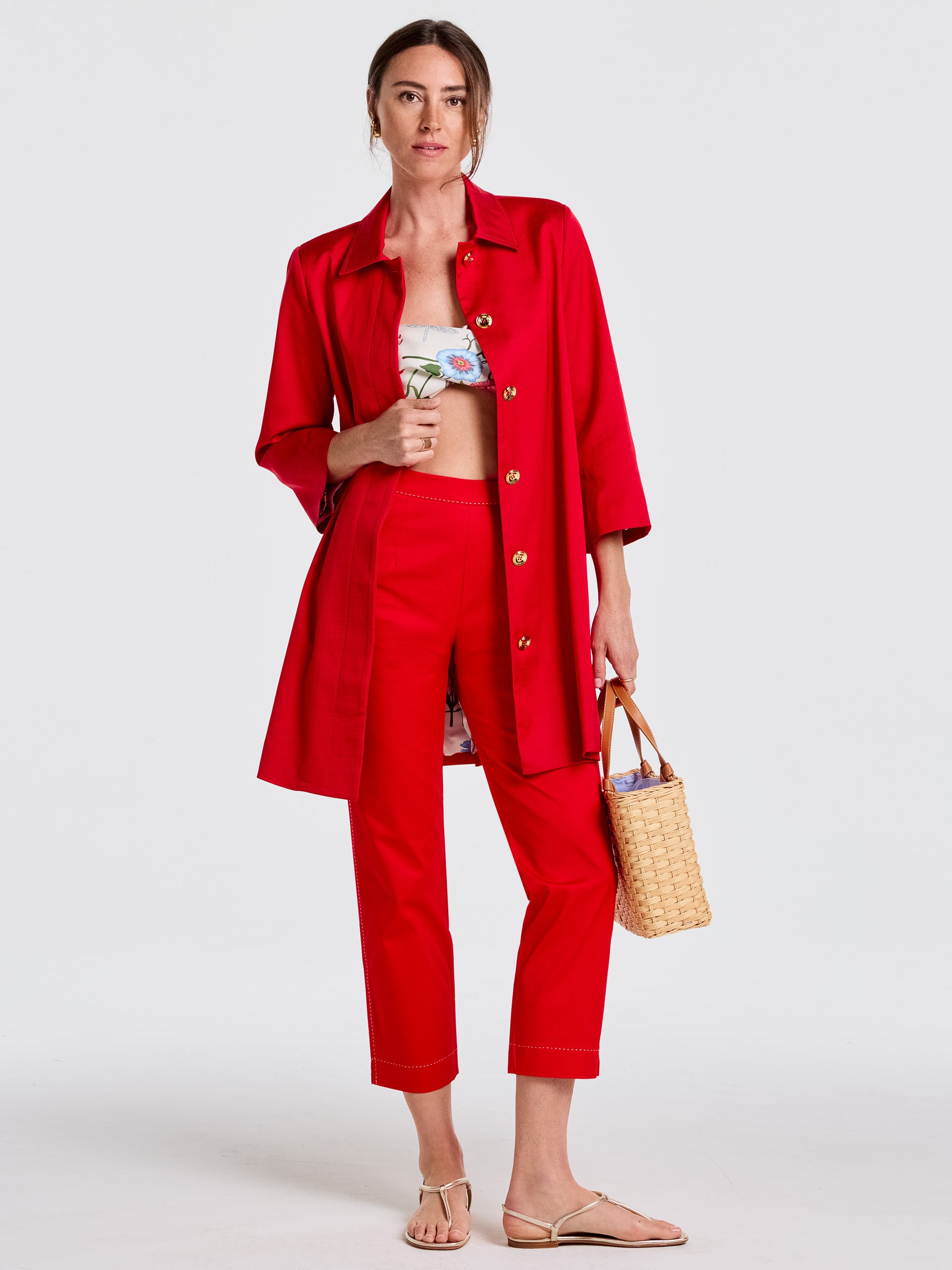 Woman wearing vibrant red Betina Pants by J.McLaughlin paired with a lightweight red coat, floral crop top, beige sandals, and a woven handbag, embodying effortlessly stylish, enduring designs with innovative fabrics for a legacy of timeless fashion. A destination for defining style. Life, Well-Lived.
