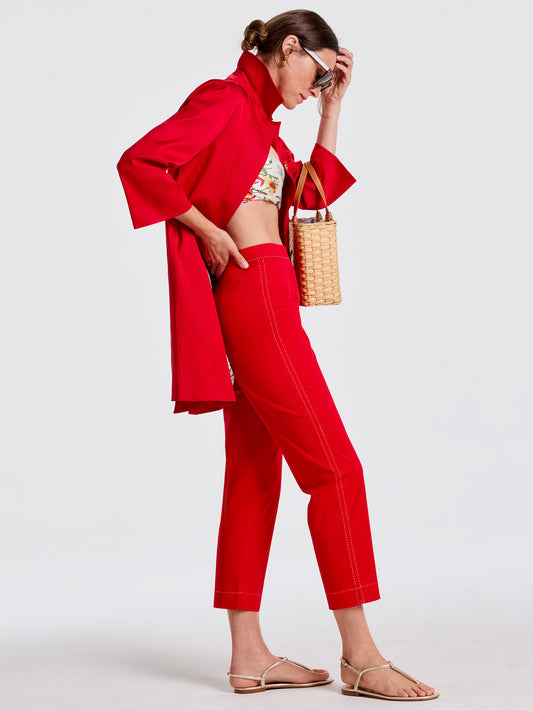 Woman wearing vibrant red Betina Pants by J.McLaughlin paired with a matching red coat and floral top, carrying a woven handbag, showcasing effortlessly stylish and enduring designs.