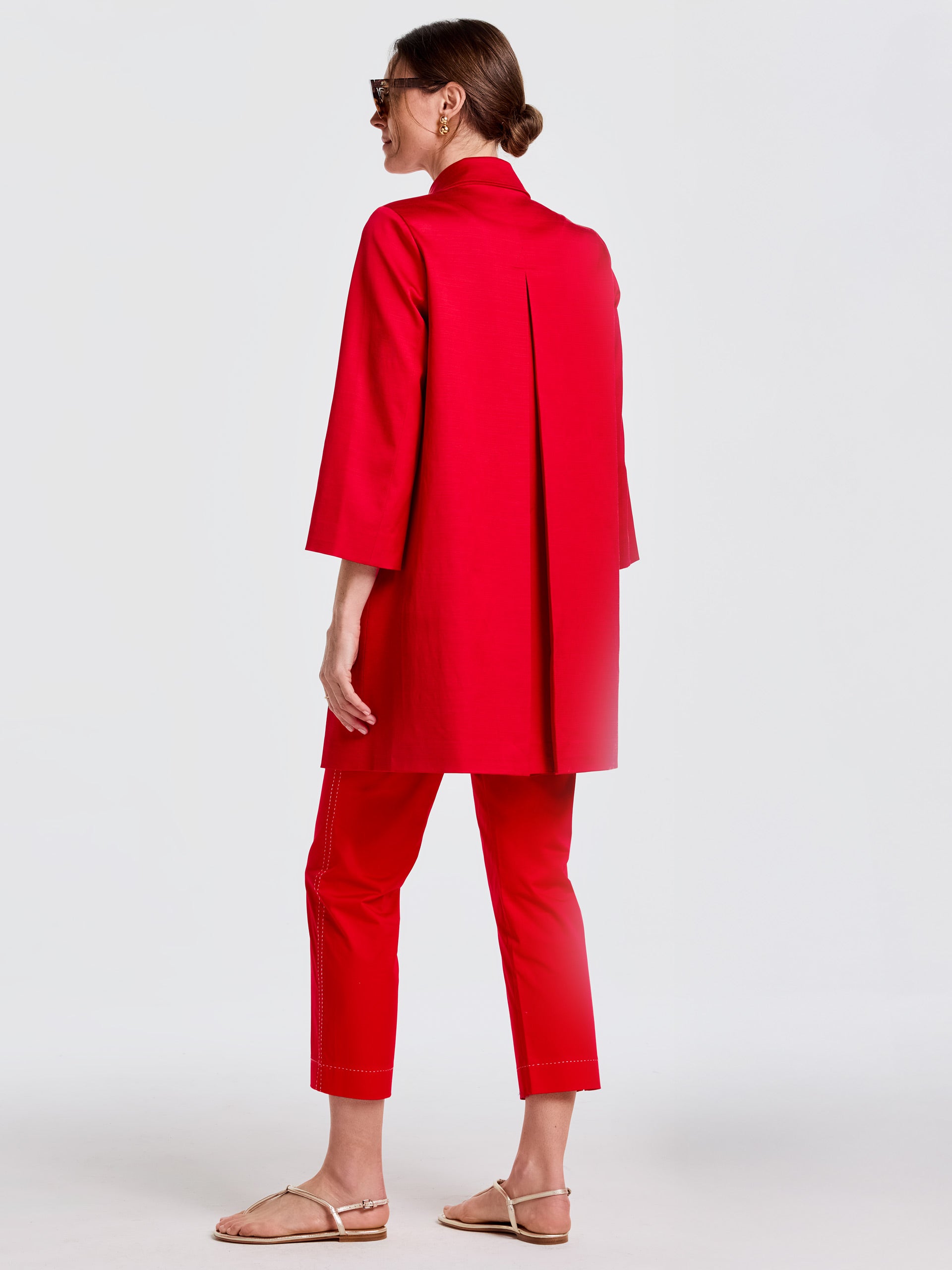 A woman models the Emma Coat by J.McLaughlin in vibrant red, pairing it with matching pants and sandals, showcasing effortlessly stylish, enduring designs and innovative fabrics in a legacy of timeless fashion. A destination for defining style. Life, Well-Lived.