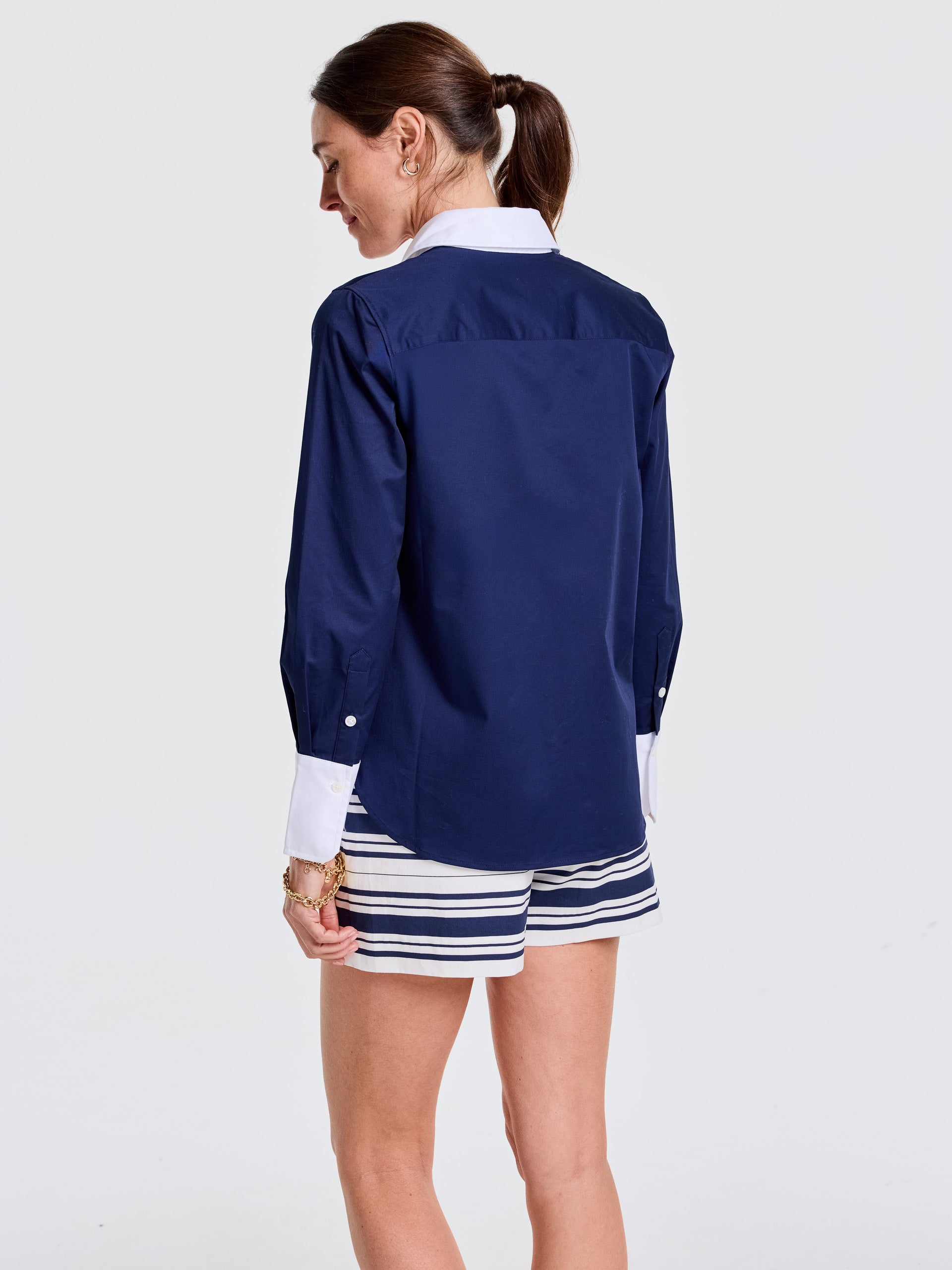 Woman wearing a J.McLaughlin Karla Shirt in navy with white collar and cuffs, paired with striped shorts, showcasing effortlessly stylish, enduring designs and innovative fabrics.
