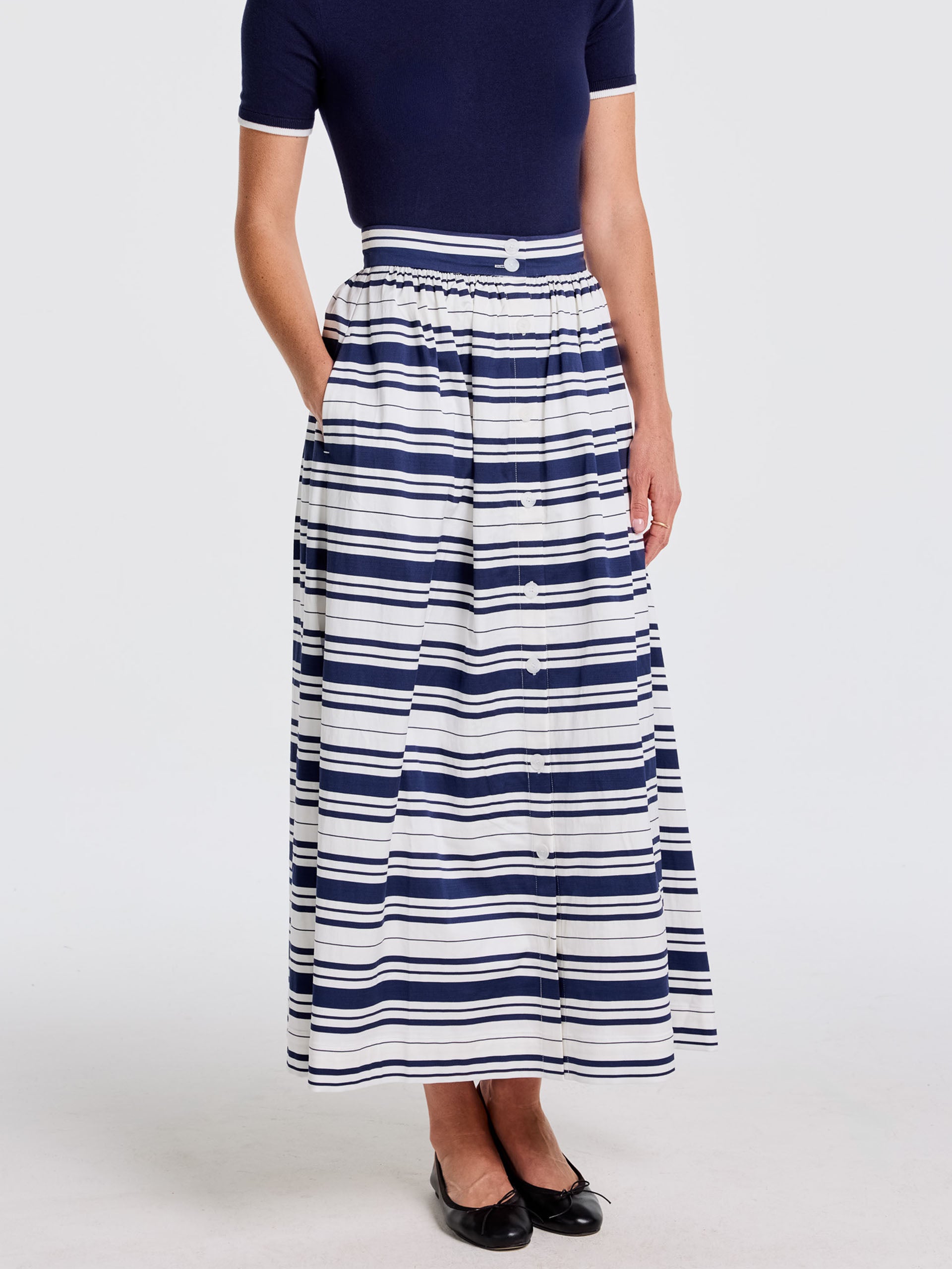 Model wearing a Susie Skirt in Mariner Stripe by J.McLaughlin paired with a navy top and black flats, showcasing effortlessly stylish, enduring designs with innovative fabrics for a timeless appeal.