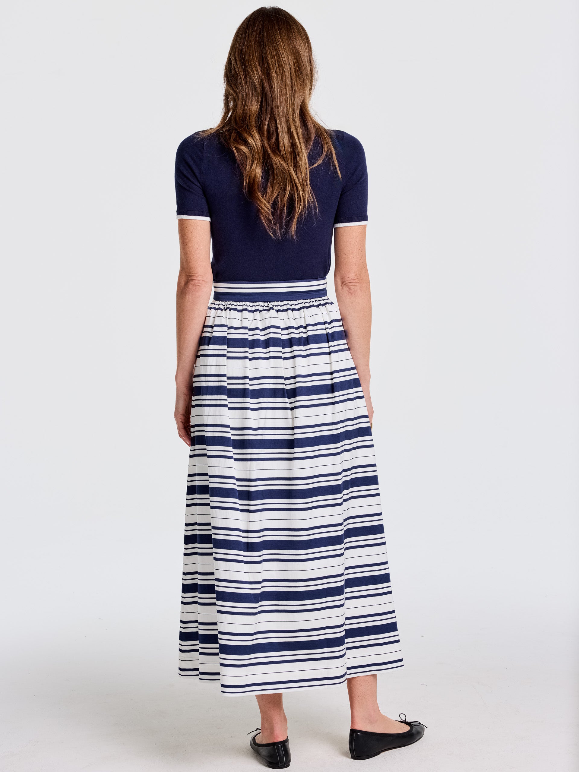 Woman wearing a Susie Skirt in Mariner Stripe by J.McLaughlin featuring bold navy and white stripes, paired with a navy short-sleeve top, showcasing effortlessly stylish, enduring designs in timeless fashion.