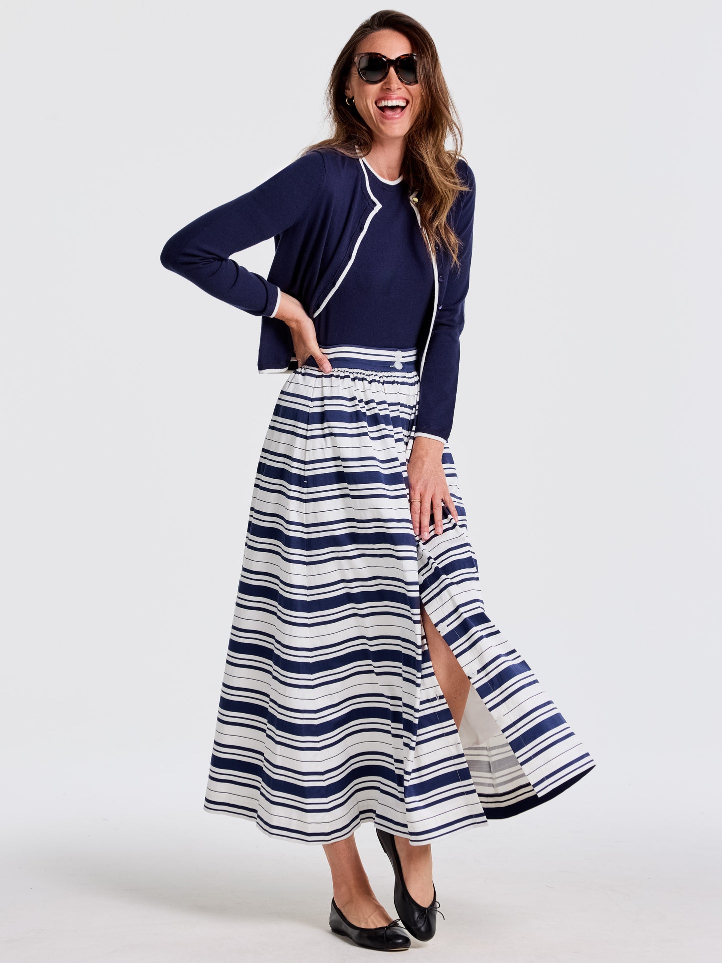 Woman wearing J. McLaughlin Susie Skirt in Mariner Stripe with a navy cardigan and black flats, embodying effortlessly stylish, enduring designs and a legacy of timeless fashion.