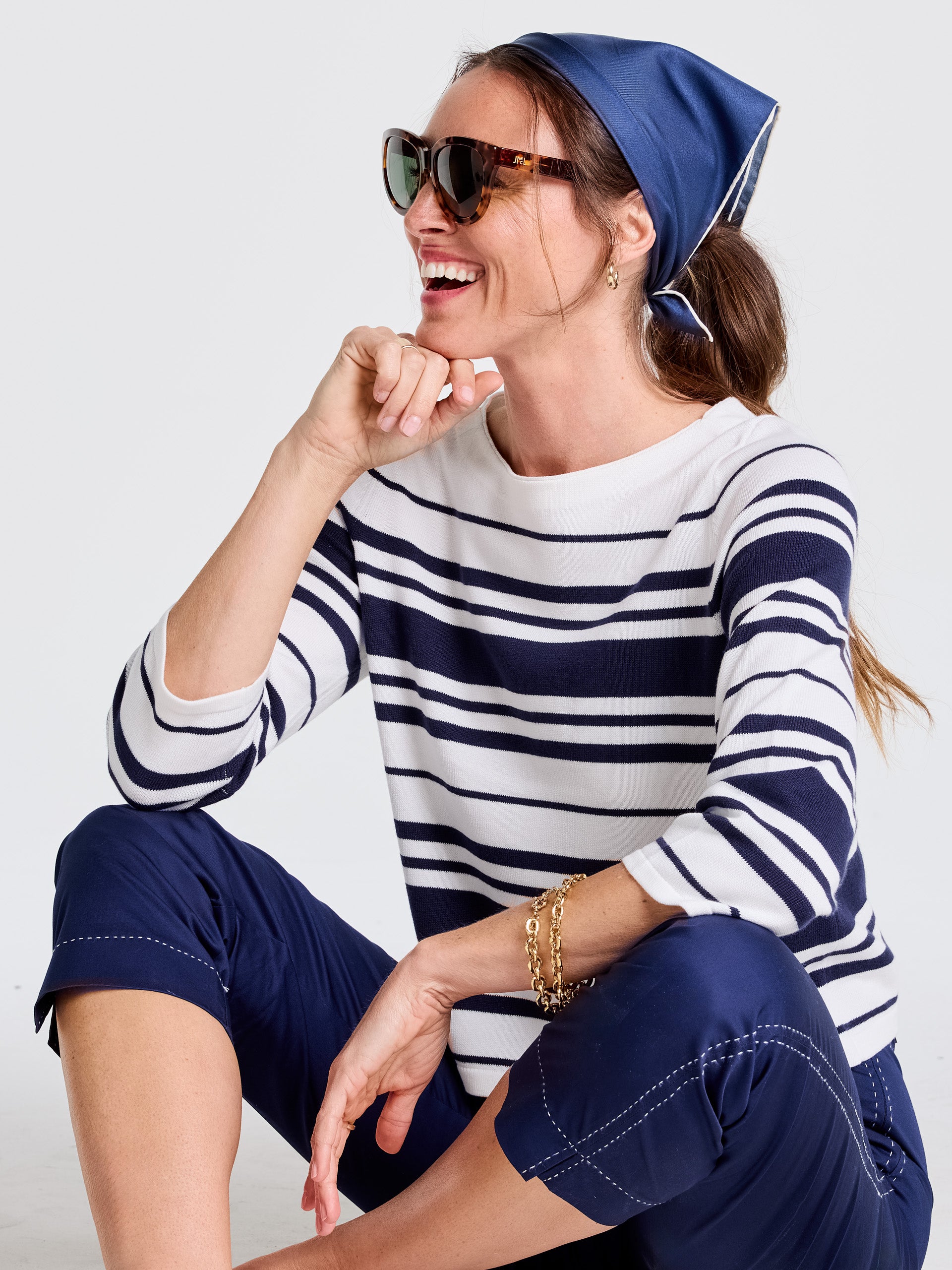 Woman wearing a navy blue Kyleigh Silk Scarf by J.McLaughlin tied around her head, paired with a classic striped top and navy pants, embodying effortlessly stylish, enduring designs and a legacy of timeless fashion. A destination for defining style. Life, Well-Lived.