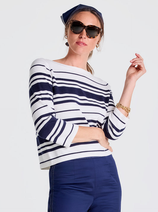 Woman wearing Ali Sweater in Mariner Stripe by J.McLaughlin, featuring classic navy and white stripes, paired with navy pants and accessorized with sunglasses, a headscarf, and gold bracelets, showcasing effortlessly stylish, enduring designs and innovative fabrics in a legacy of timeless fashion. A destination for defining style. Life, Well-Lived.