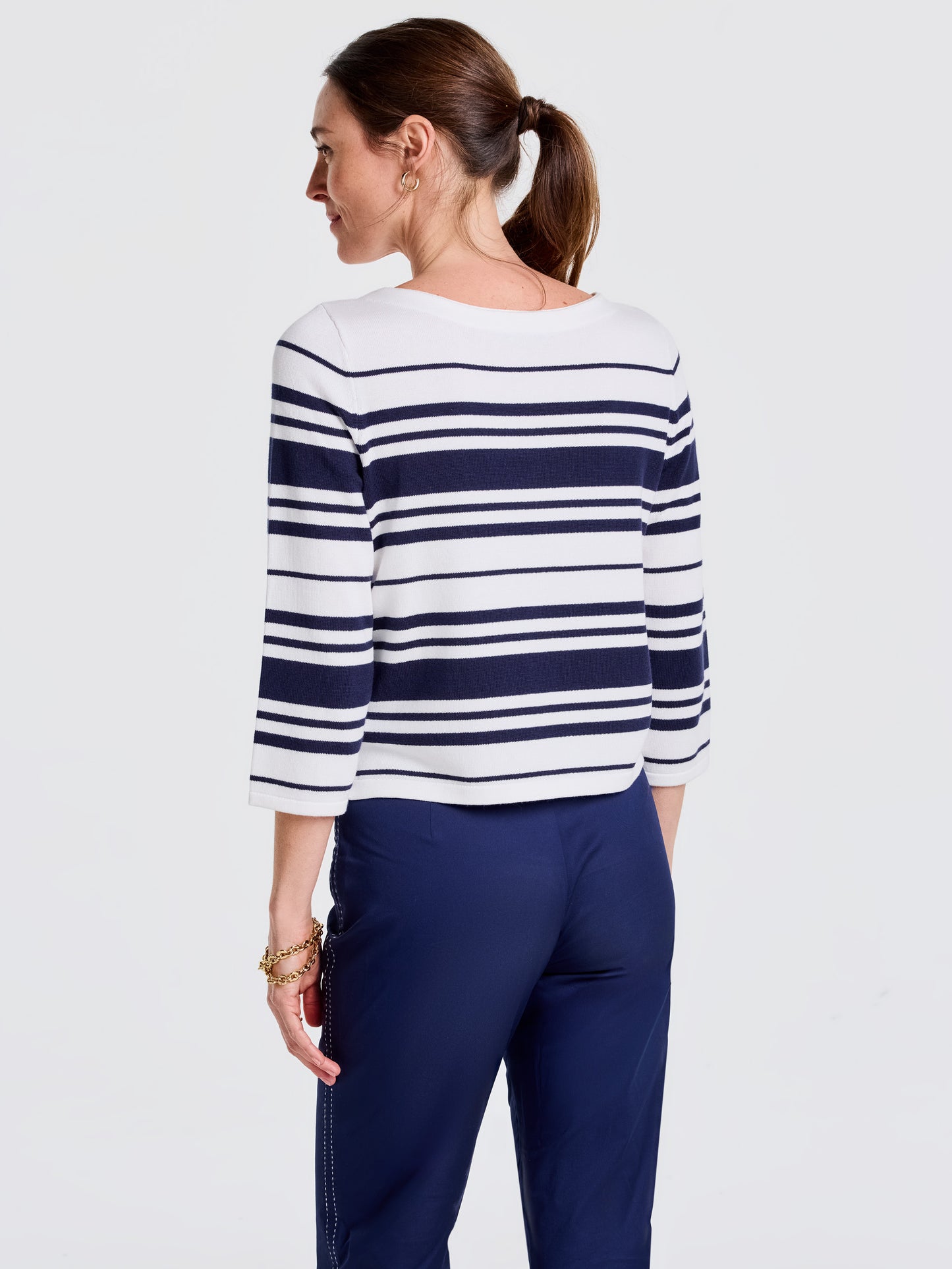 Woman wearing an Ali Sweater in Mariner Stripe by J.McLaughlin paired with navy pants, showcasing effortlessly stylish, enduring designs and a legacy of timeless fashion.