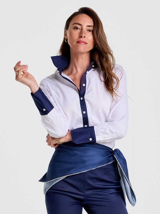 A confident woman models the Karla Shirt by J.McLaughlin, featuring crisp white fabric with deep navy collar, cuffs, and button placket, embodying effortlessly stylish, enduring designs in a legacy of timeless fashion. A destination for defining style. Life, Well-Lived.