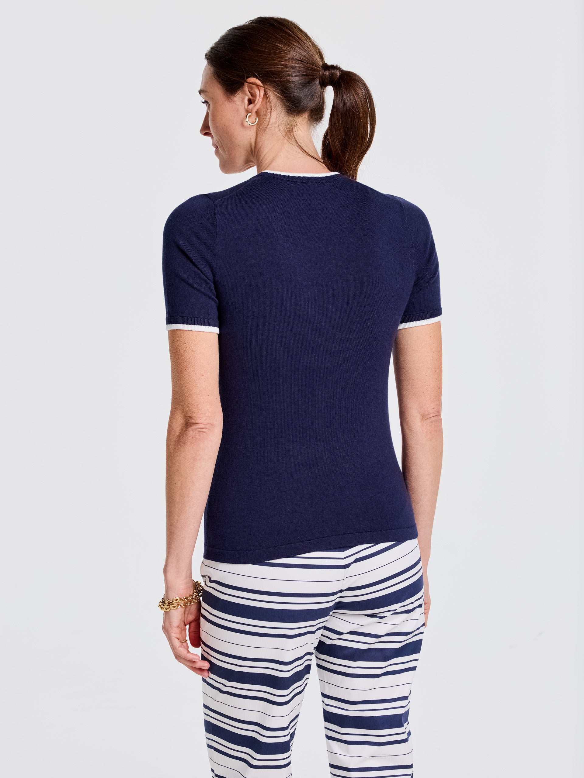 Woman wearing a navy Alyson Sweater Tee by J.McLaughlin, paired with white and navy striped pants, showcasing effortlessly stylish, enduring designs and innovative fabrics.