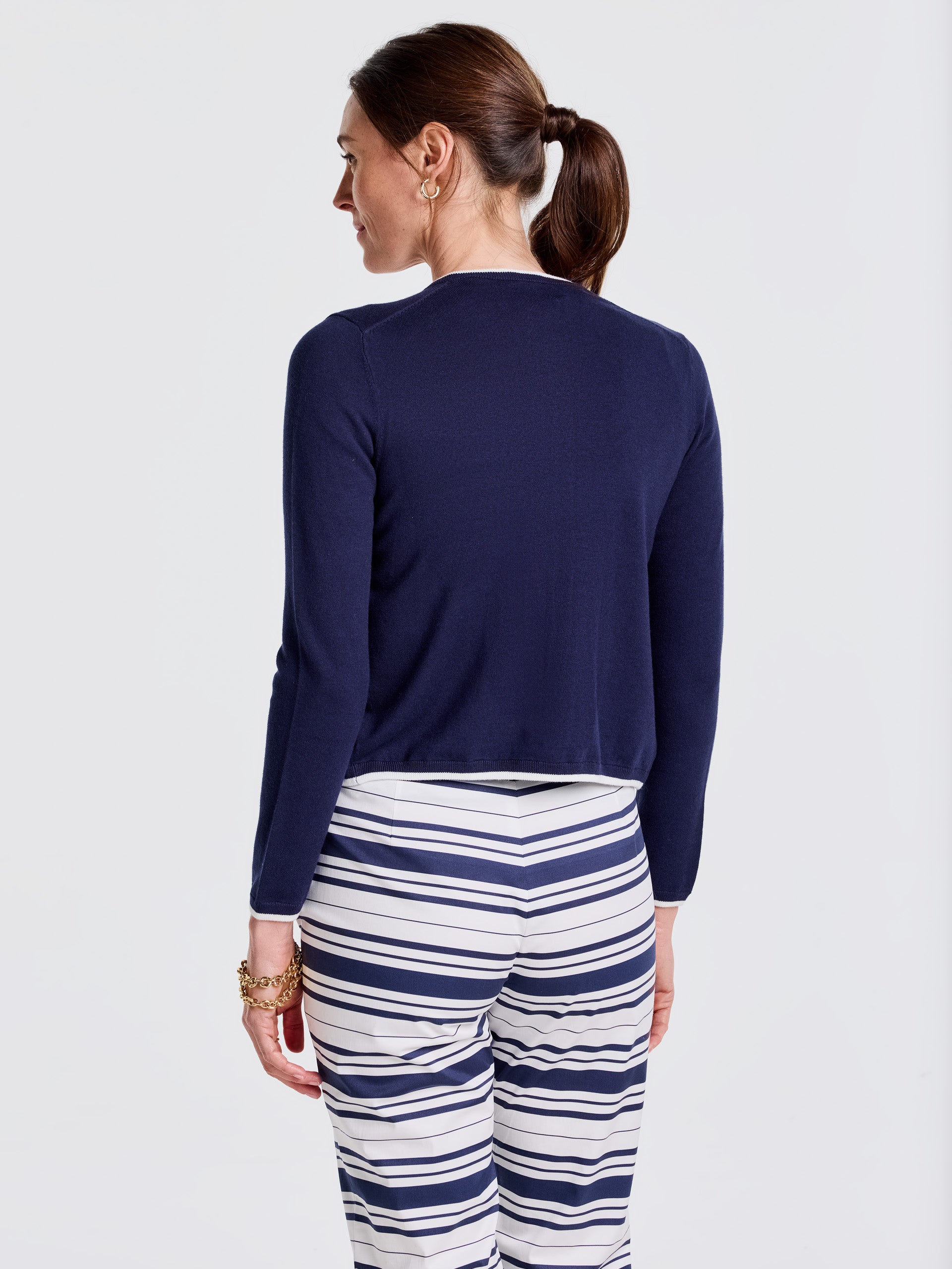 Woman wearing a navy Aileen Cardigan with long sleeves paired with white and navy striped pants, showcasing J.McLaughlin's effortlessly stylish, enduring designs and legacy of timeless fashion.