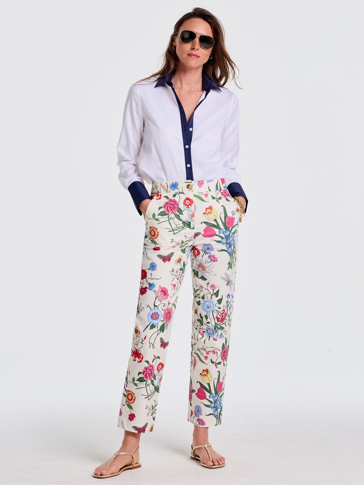 Woman wearing a white blouse with navy trim, paired with Avery Pants in Dragonfly Garden featuring a vibrant floral print, styled effortlessly with sandals and sunglasses by J.McLaughlin, embodying enduring designs and a legacy of timeless fashion. A destination for defining style. Life, Well-Lived.