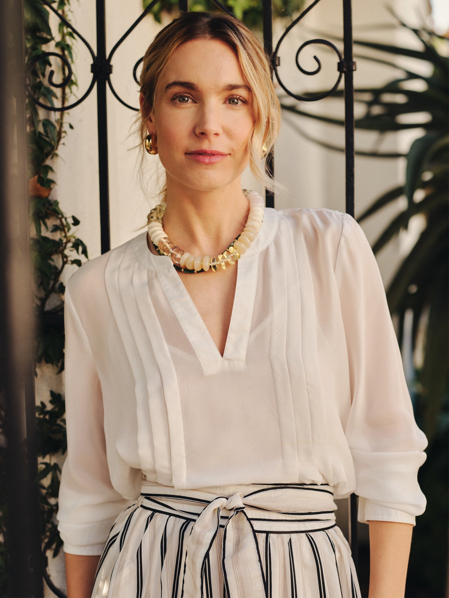 Woman wearing a Katherine Silk Chiffon Blouse by J.McLaughlin, styled with a striped tied skirt and statement necklace, embodying effortlessly stylish, enduring designs with innovative fabrics.