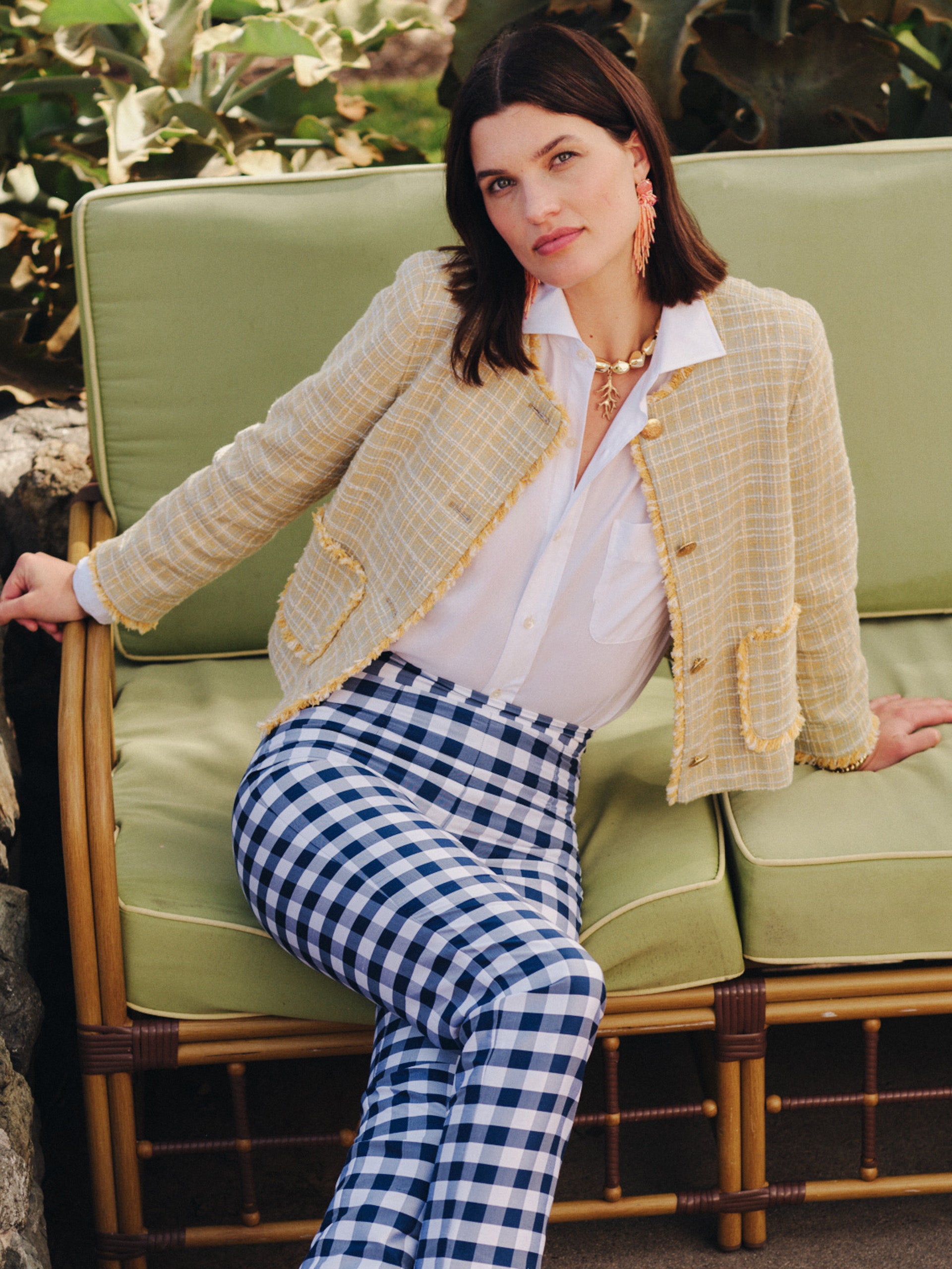Woman seated on outdoor bench wearing a cream and yellow Abigail Bouclé Jacket in Mini Window Pane by J.McLaughlin over a white blouse, paired with blue checkered pants, showcasing effortlessly stylish, enduring designs and a legacy of timeless fashion at a destination for defining style. Life, Well-Lived.