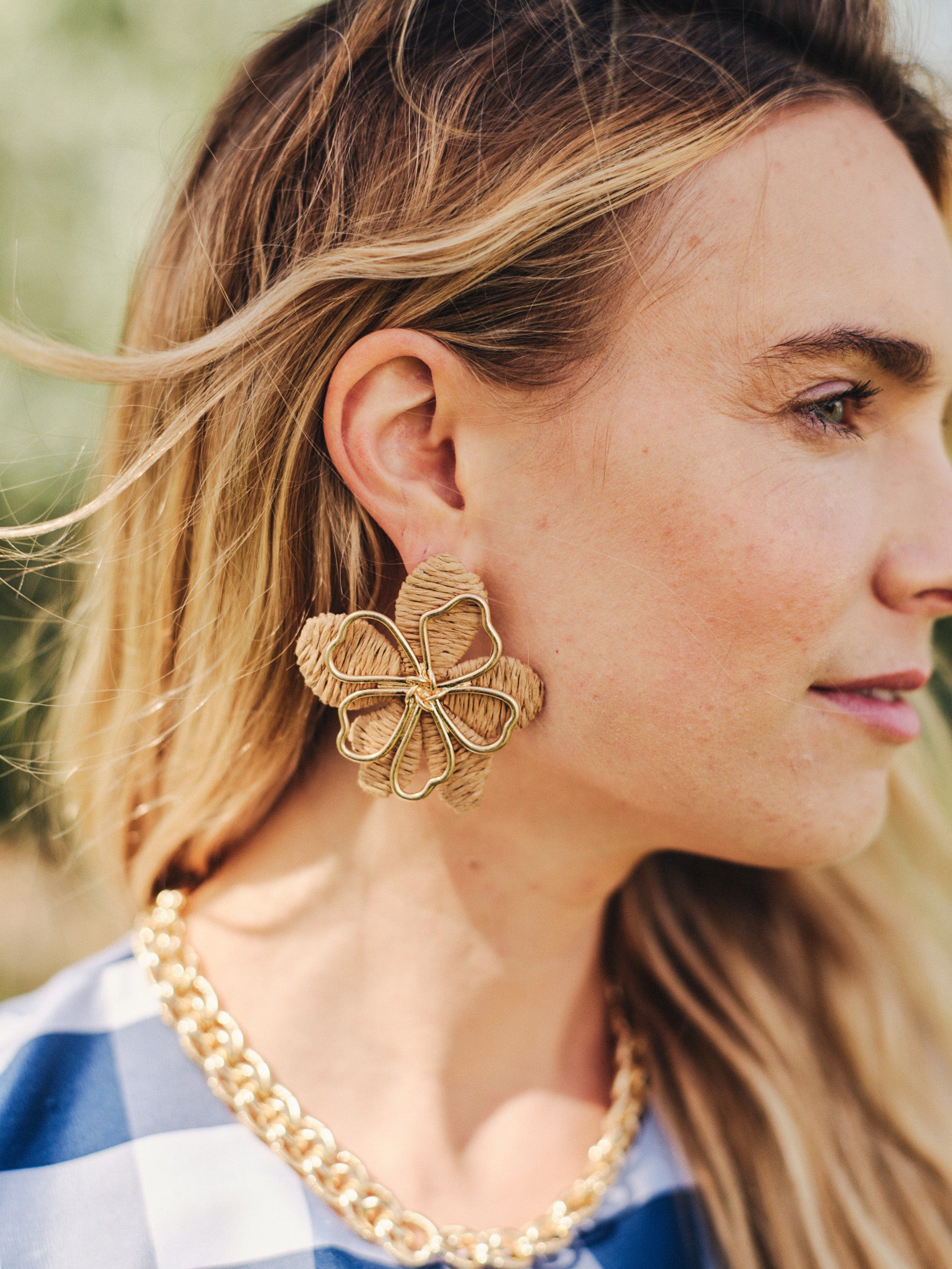 Close-up of a woman wearing J.McLaughlin Flower Earrings with a bold floral design, paired with a gold chain necklace, embodying effortlessly stylish, enduring designs and a legacy of timeless fashion.