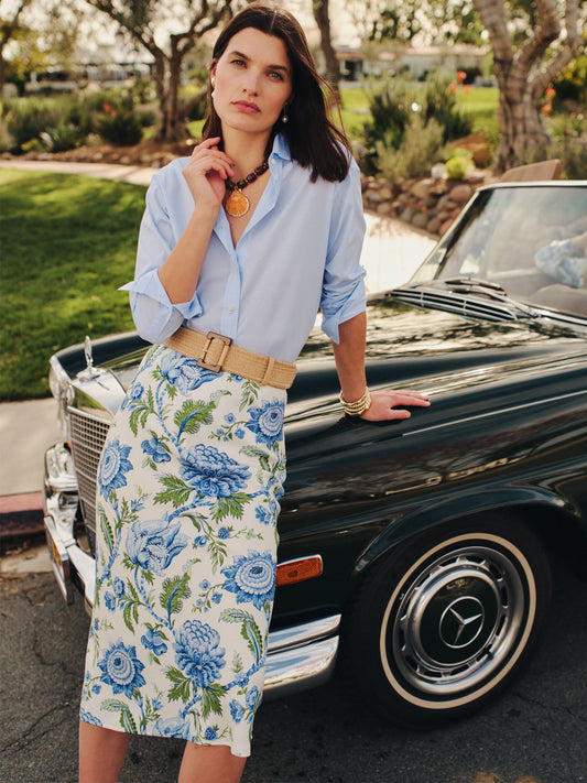 Woman wearing a blue button-up shirt tucked into an Adelyn Silk Blend Skirt in Cerulean Garden Bias by J.McLaughlin, leaning against a vintage black Mercedes car, embodying effortlessly stylish, enduring designs with a legacy of timeless fashion. A destination for defining style. Life, Well-Lived.