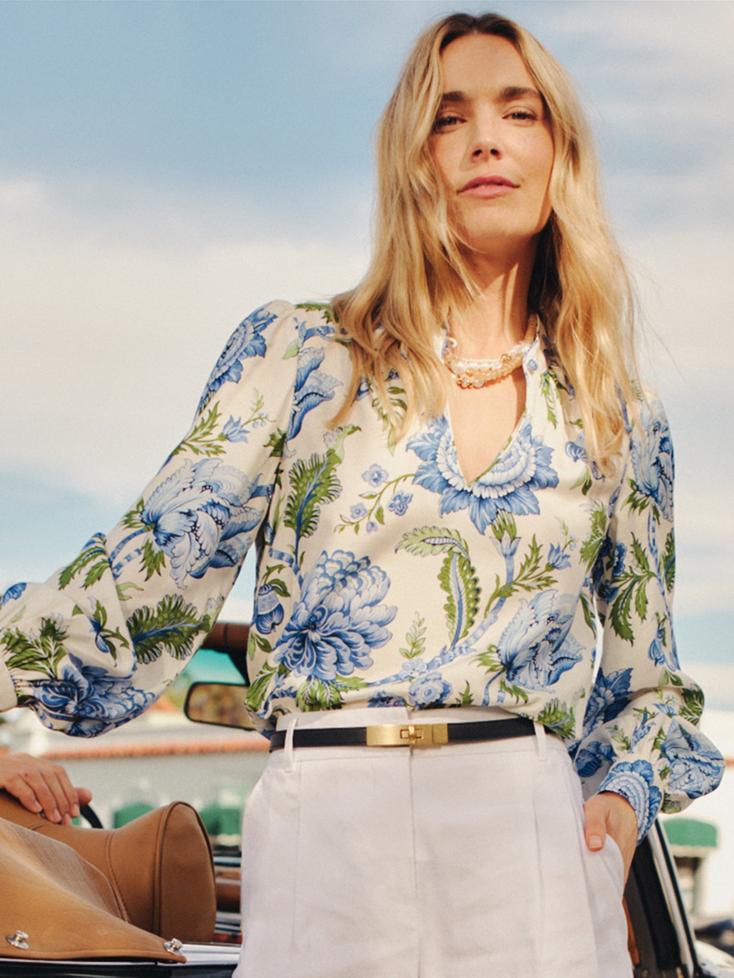 Woman wearing a Maeve Silk Blend Blouse in Cerulean Garden with blue floral pattern and billowed sleeves paired with white pants and a black belt, styled by J.McLaughlin, showcasing effortlessly stylish, enduring designs and innovative fabrics for a legacy of timeless fashion. A destination for defining style. Life, Well-Lived.