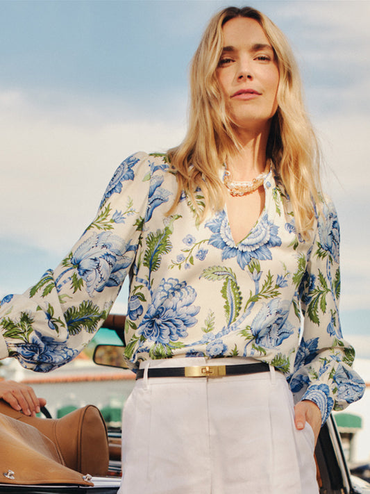Woman wearing a Maeve Silk Blend Blouse in Cerulean Garden with blue floral pattern and billowed sleeves paired with white pants and a black belt, styled by J.McLaughlin, showcasing effortlessly stylish, enduring designs and innovative fabrics for a legacy of timeless fashion. A destination for defining style. Life, Well-Lived.