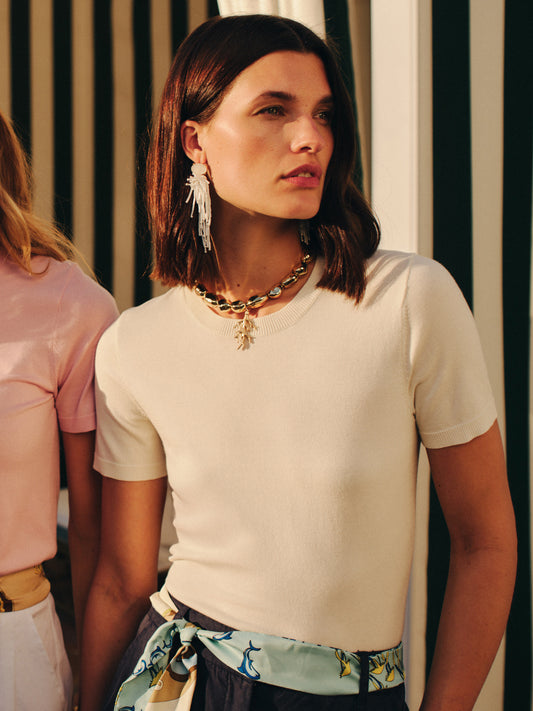 Woman wearing a cream Joelle Sweater by J.McLaughlin paired with statement earrings and a chunky necklace, embodying effortlessly stylish, enduring designs with innovative fabrics.