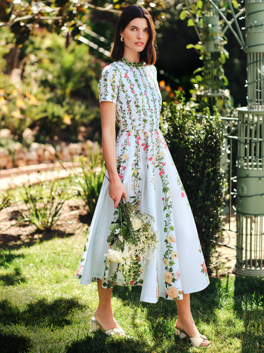 Woman in a Grace Dress in Floral Medley Ray by J.McLaughlin stands outdoors holding flowers, showcasing effortlessly stylish, enduring designs with a legacy of timeless fashion.