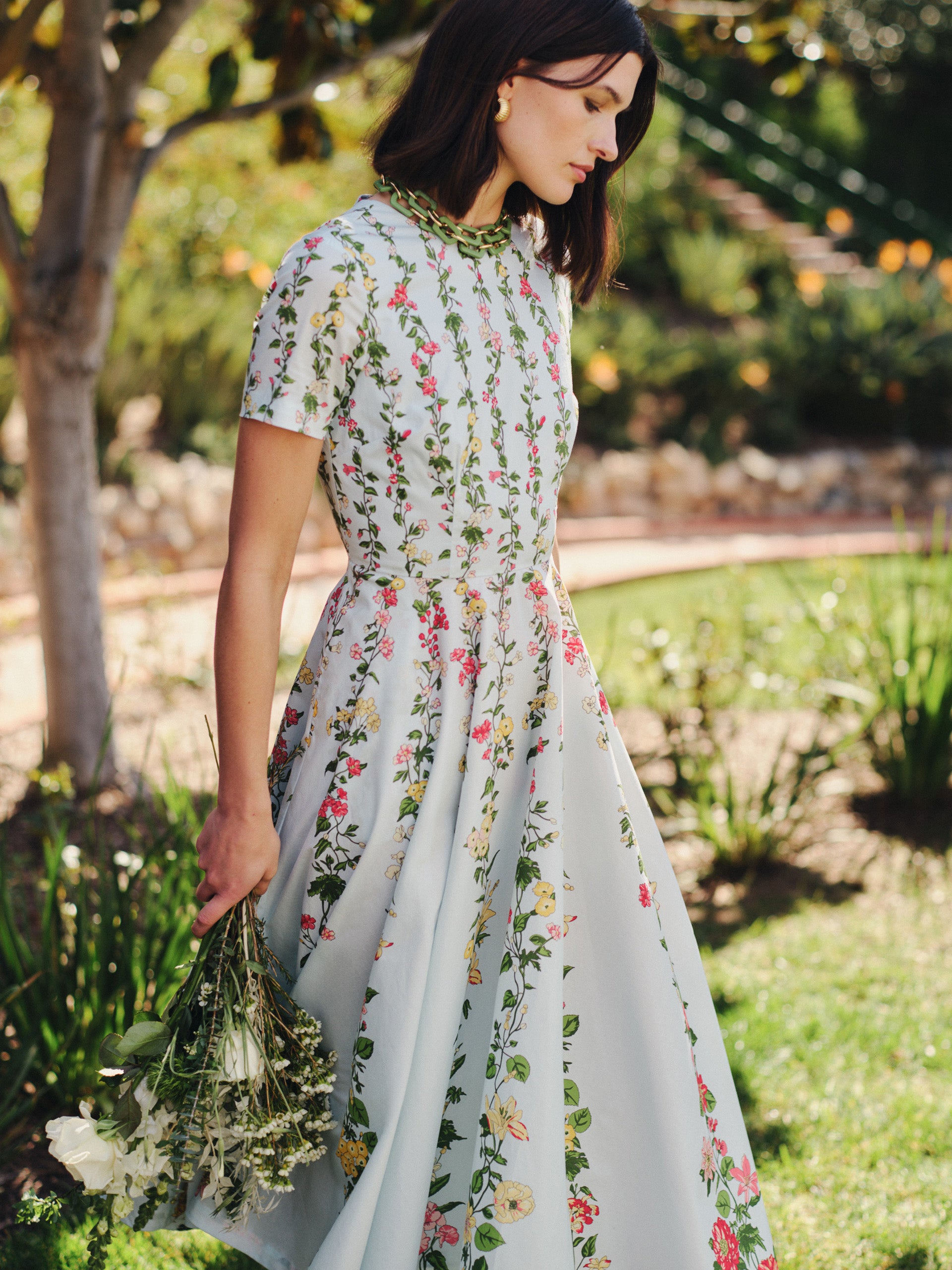 A woman in a Grace Dress in Floral Medley Ray by J.McLaughlin, featuring effortlessly stylish floral patterns and enduring designs in an outdoor garden setting.
