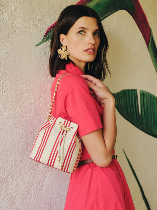 Woman wearing a vibrant red dress with flower-shaped earrings carrying a Daisy Canvas Bucket Bag in Stripe by J.McLaughlin, showcasing effortlessly stylish accessories and enduring designs.